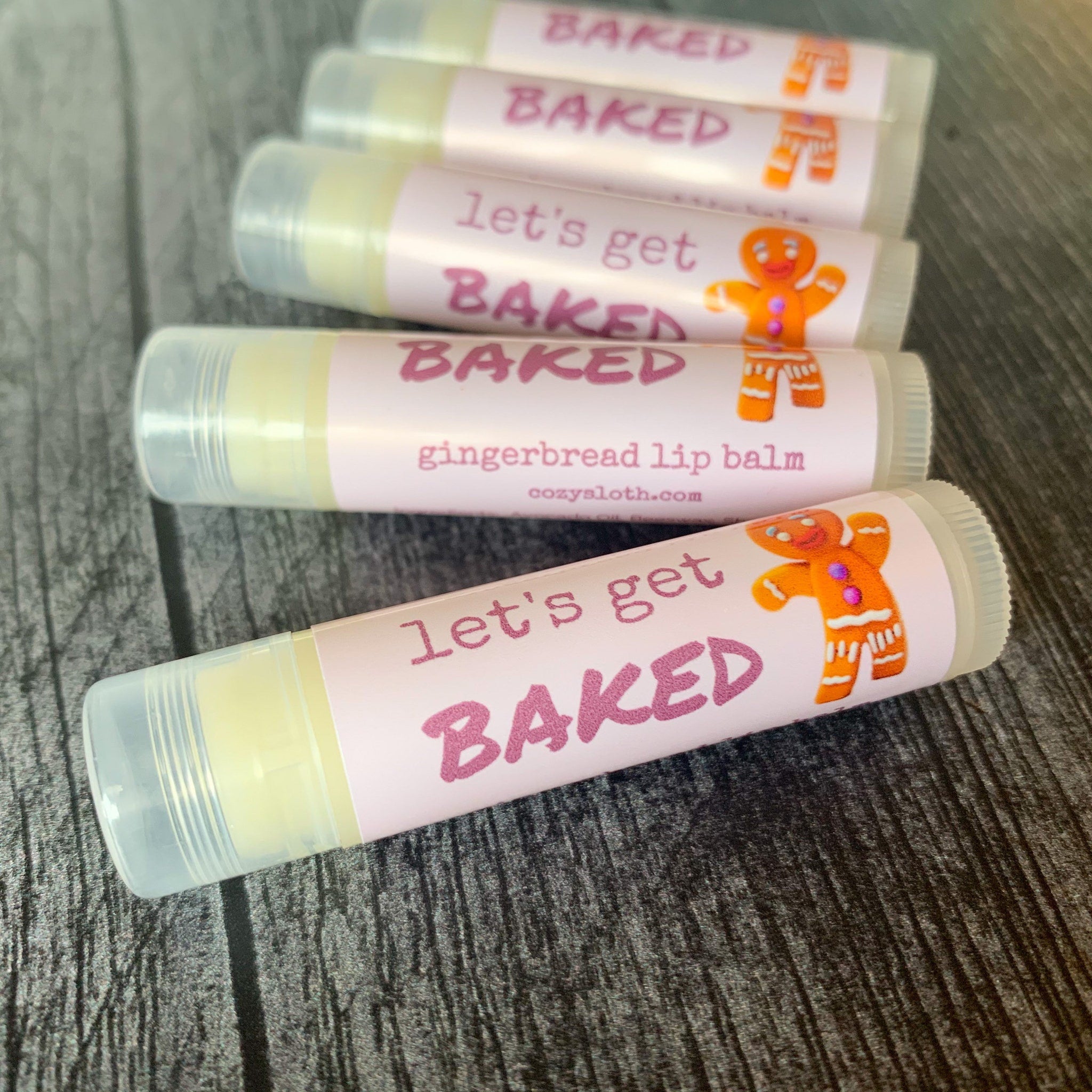 Lip balm tubes with pink labels, gingerbread man design, and clear caps, "BAKED" text