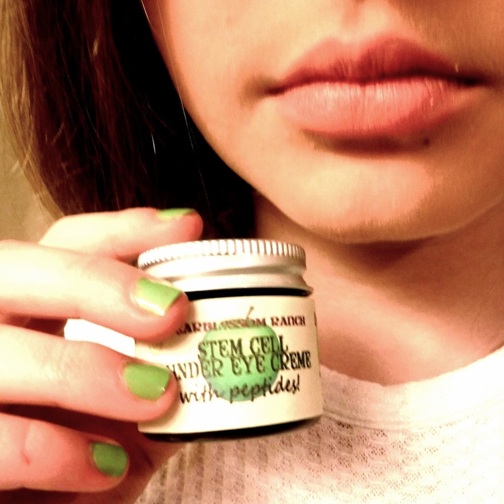 Eye cream jar with silver lid, white label, and green nail polish on fingers holding it