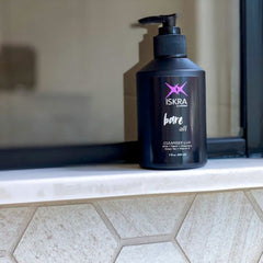 Cleanser bottle with black pump, purple and white text, on a white ledge and patterned tile