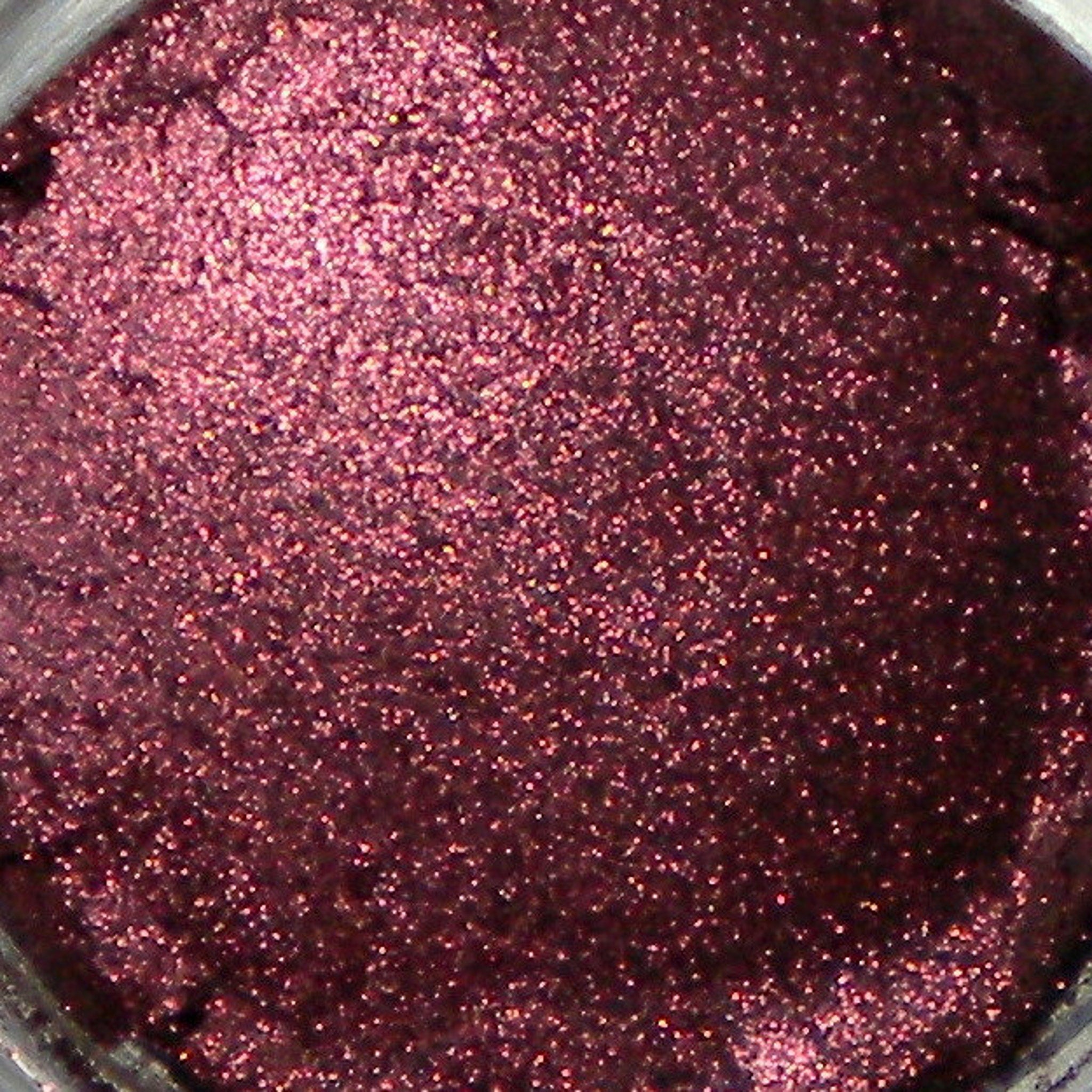 Close-up of pomegranate-hued mineral eyeshadow in sample container with vegan label, showcasing fine shimmer texture
