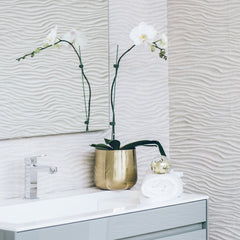 White orchid flowers with green stems in a gold pot on a bathroom vanity with a white towel