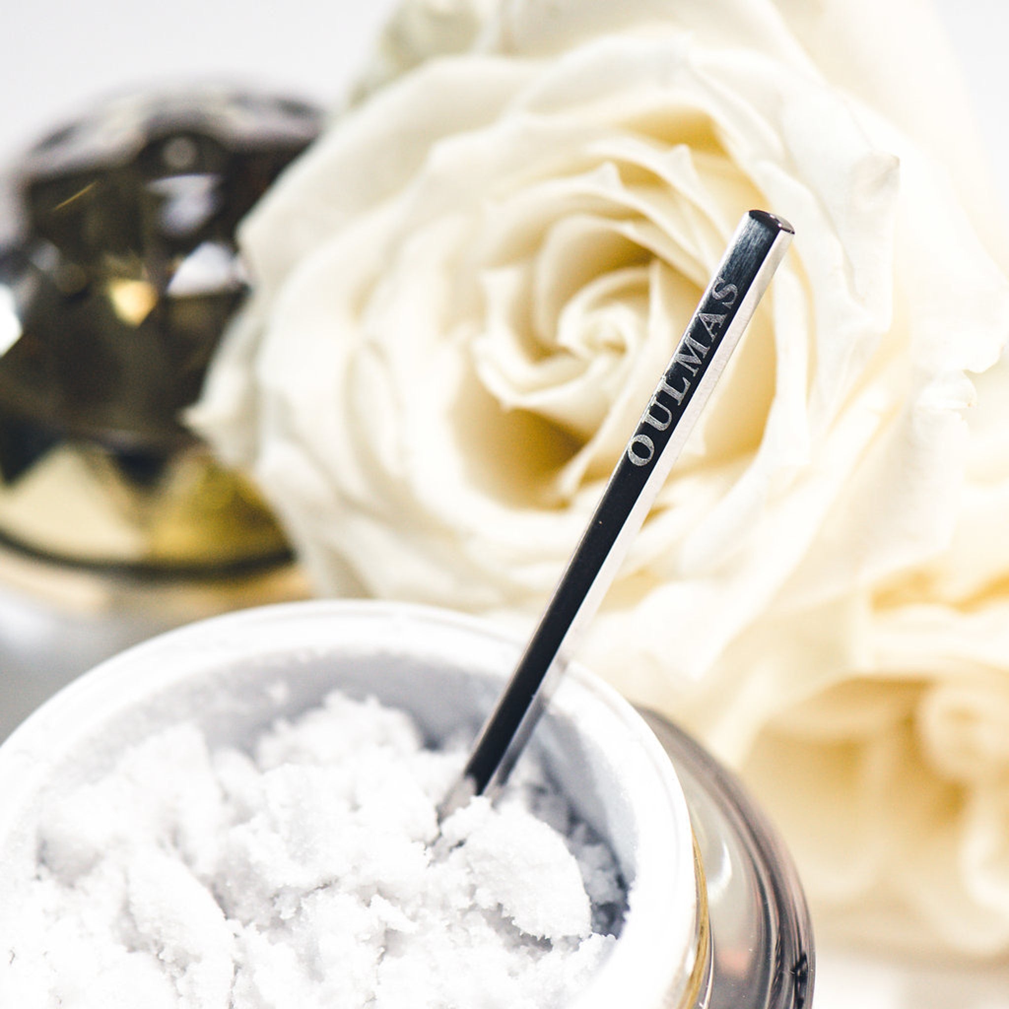 Spoon with OULMAS text, silver metal, white powder in container, with white roses in background