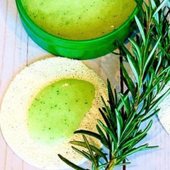 Green scrub with green container and rosemary sprig on white surface