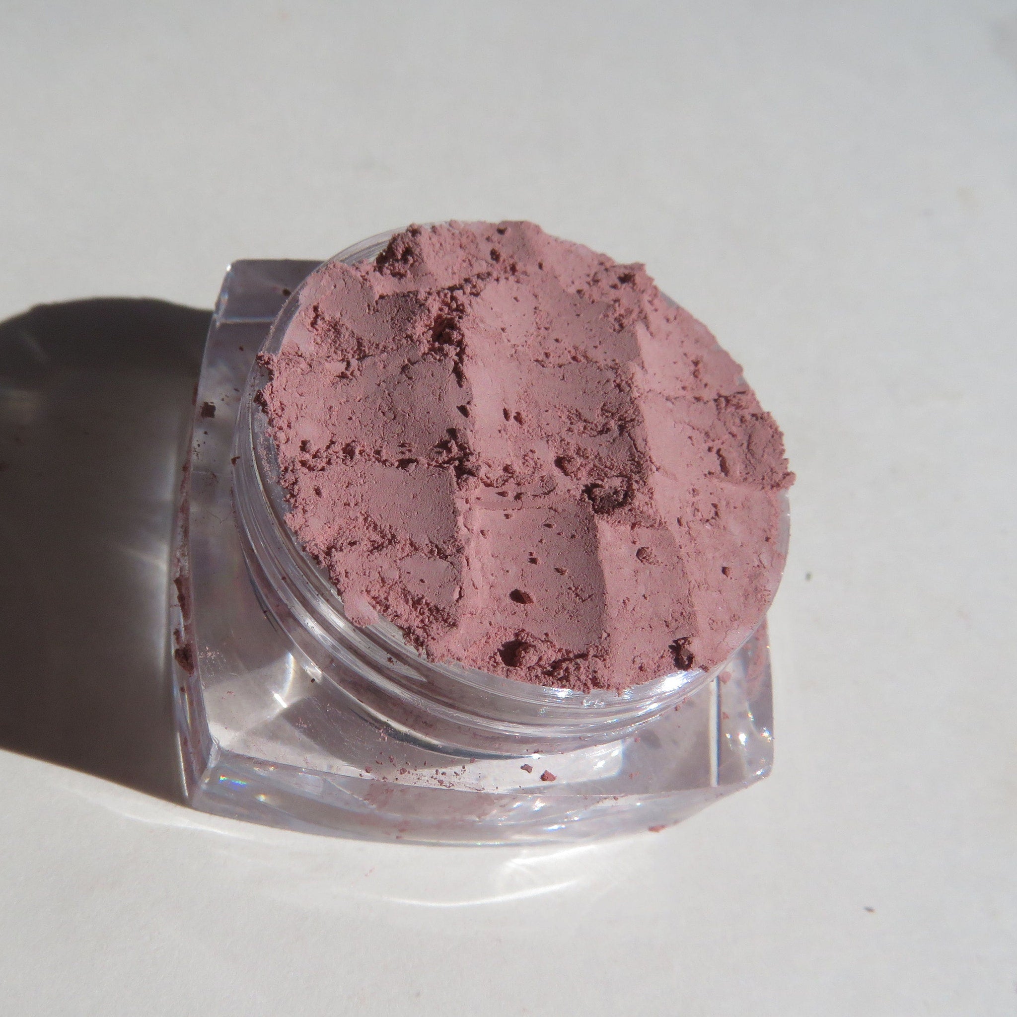 Pink mineral eyeshadow pot with matte finish, shown open on a marble surface with brush applicator