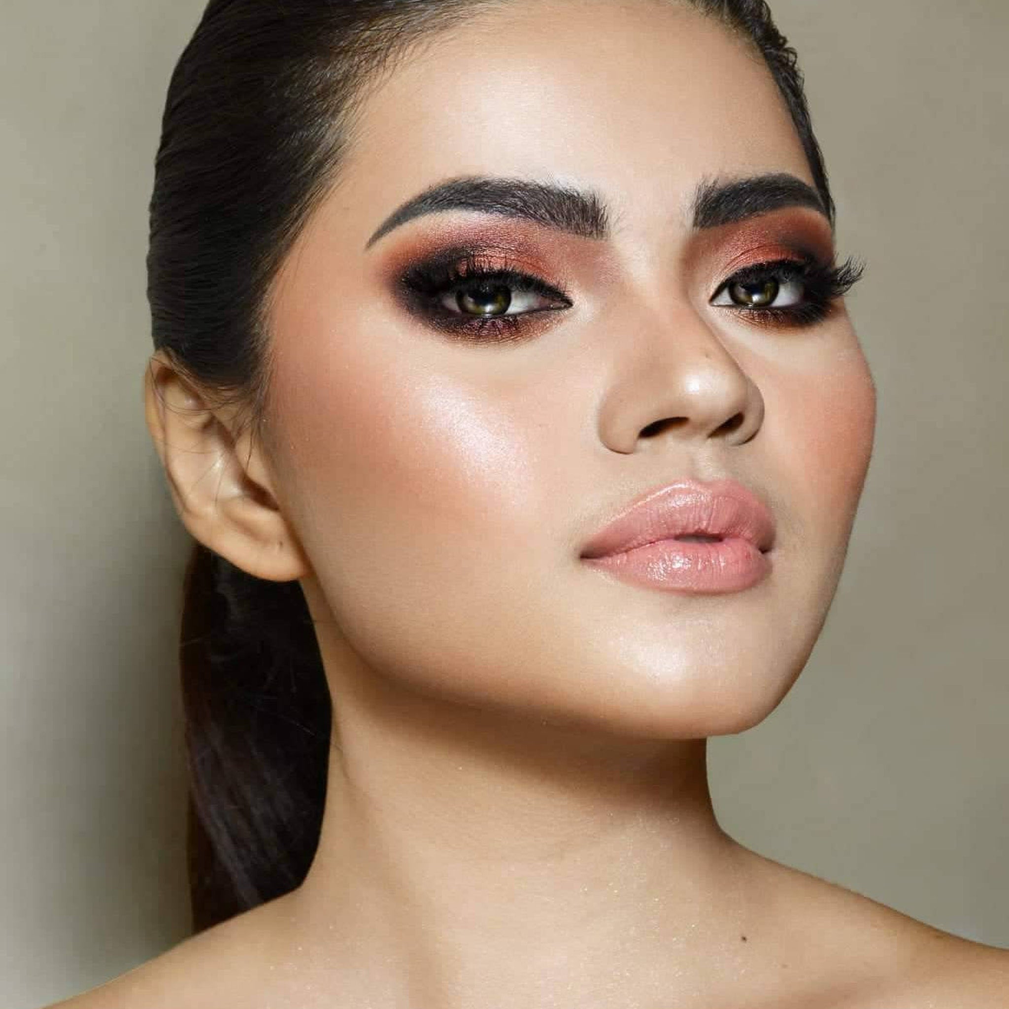 Hand applying shimmery taupe eyeshadow from palette with a fluffy brush onto eyelid
