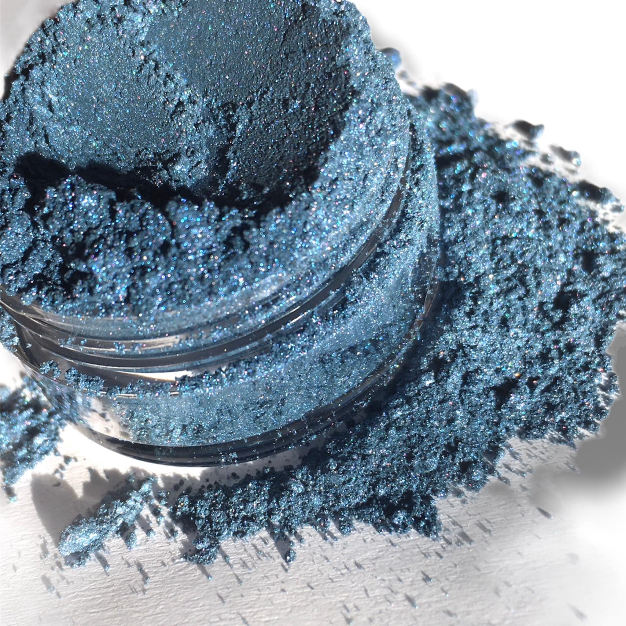 Blue eyeshadow powder with shimmer and loose texture, in a small jar and spilled out