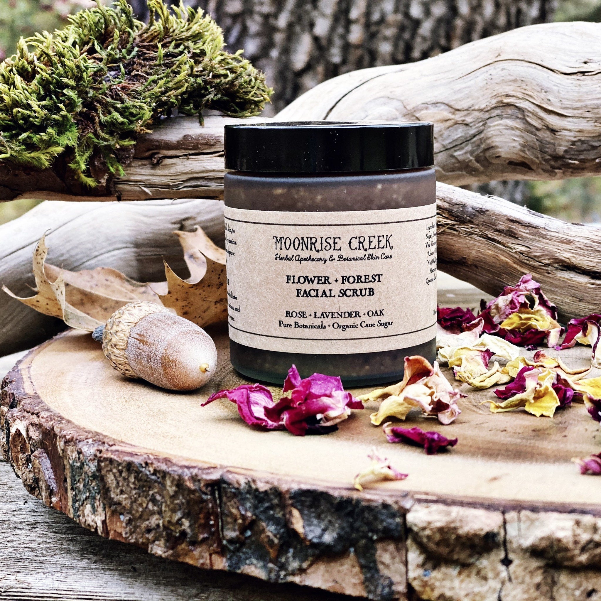 Facial scrub jar with black lid, Moonrise Creek label, and dried flower petals on wood