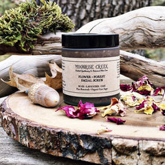 Facial scrub jar with black lid, Moonrise Creek label, and dried flower petals on wood