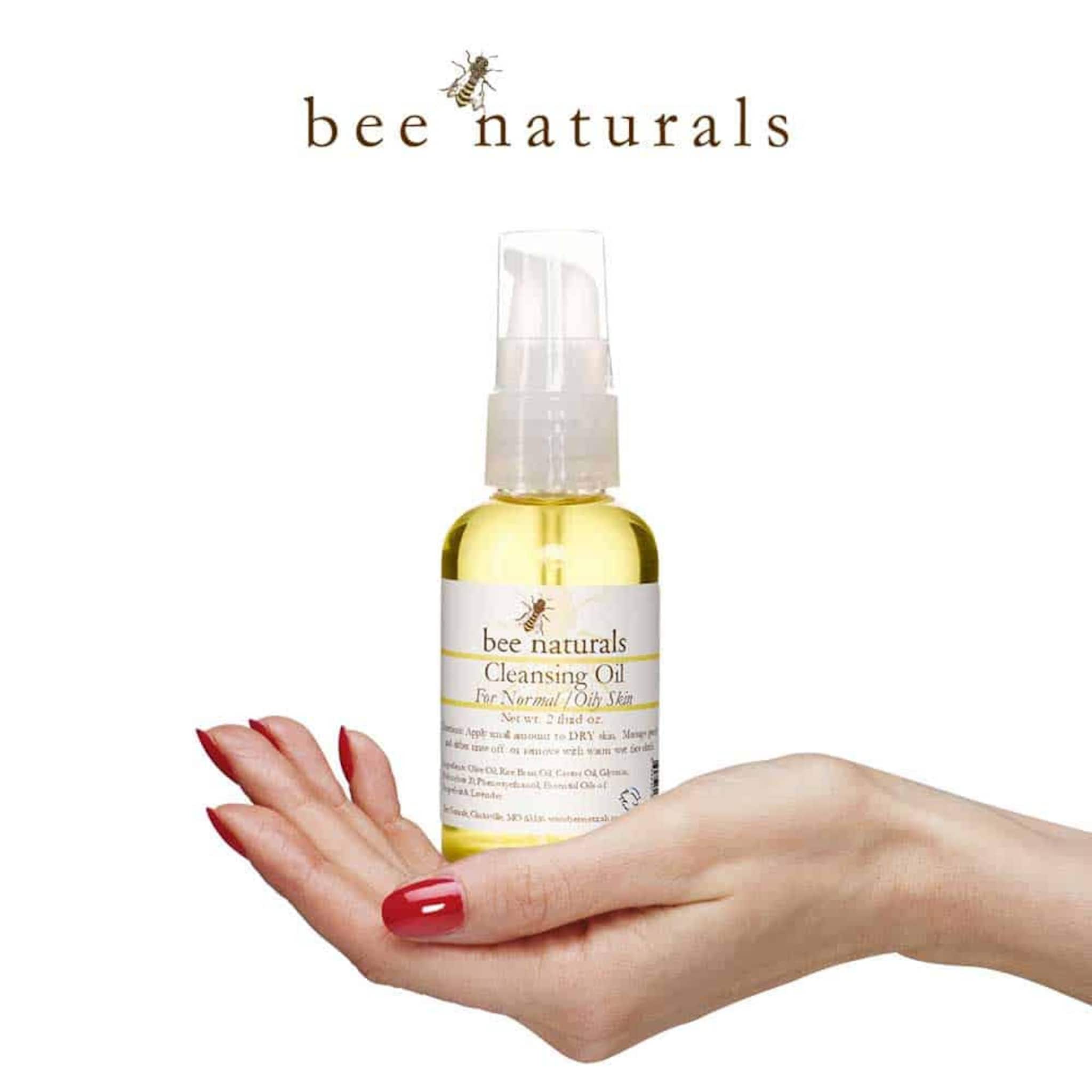 Cleansing oil bottle with yellow liquid, clear pump, and white label held in hand with red nails, Bee Naturals brand visible
