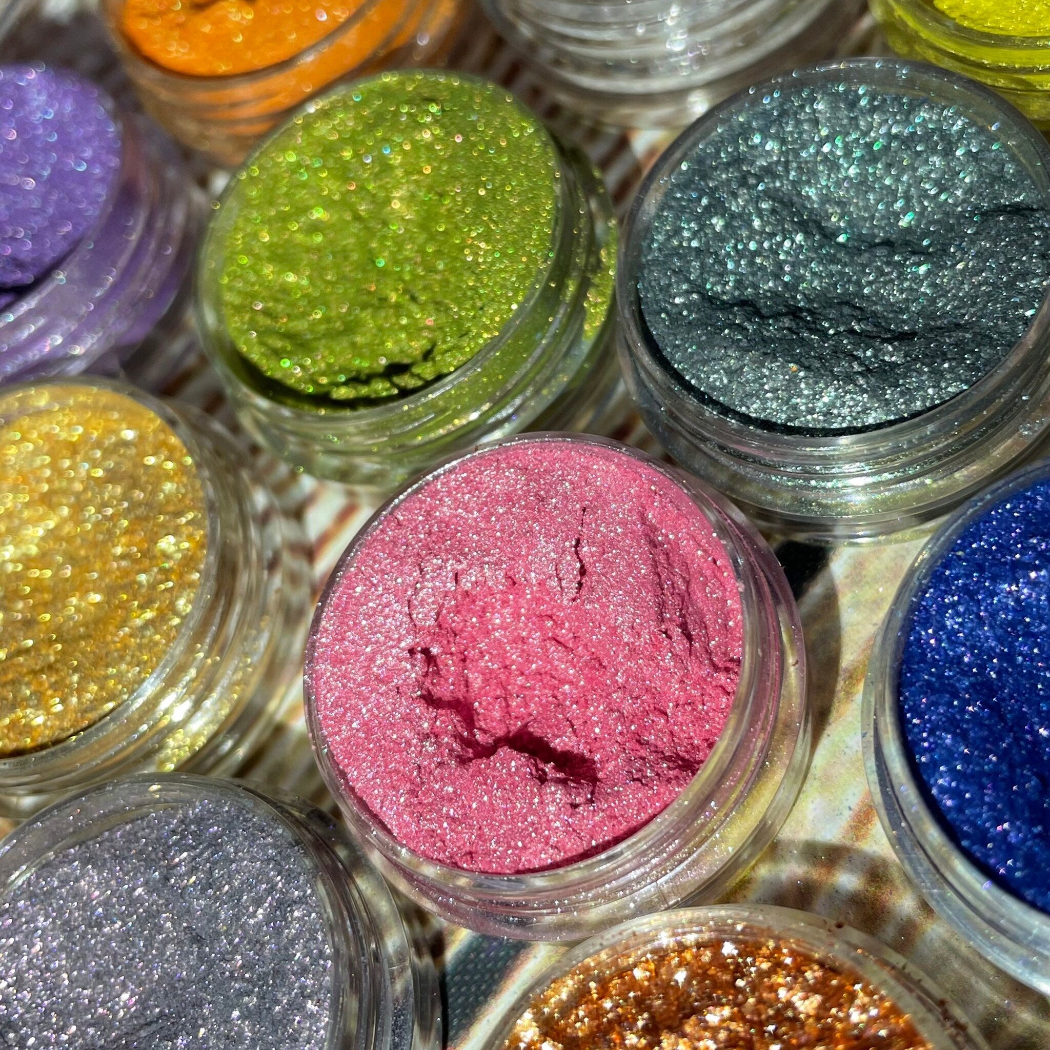 Side view of 12 shimmery vegan eyeshadows in round pans showcasing metallic and satin finishes.