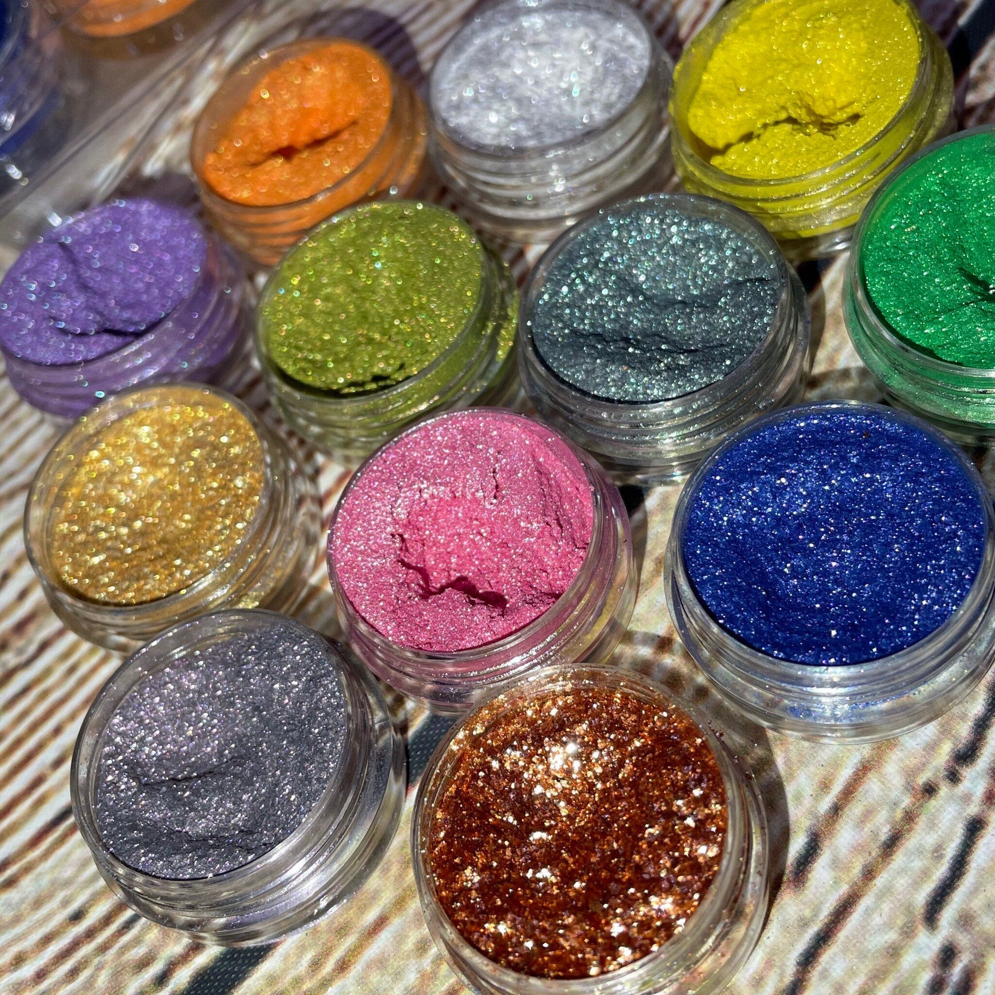 Twelve shimmery vegan eyeshadows in round pans arranged in sleek black palette with gold accents.