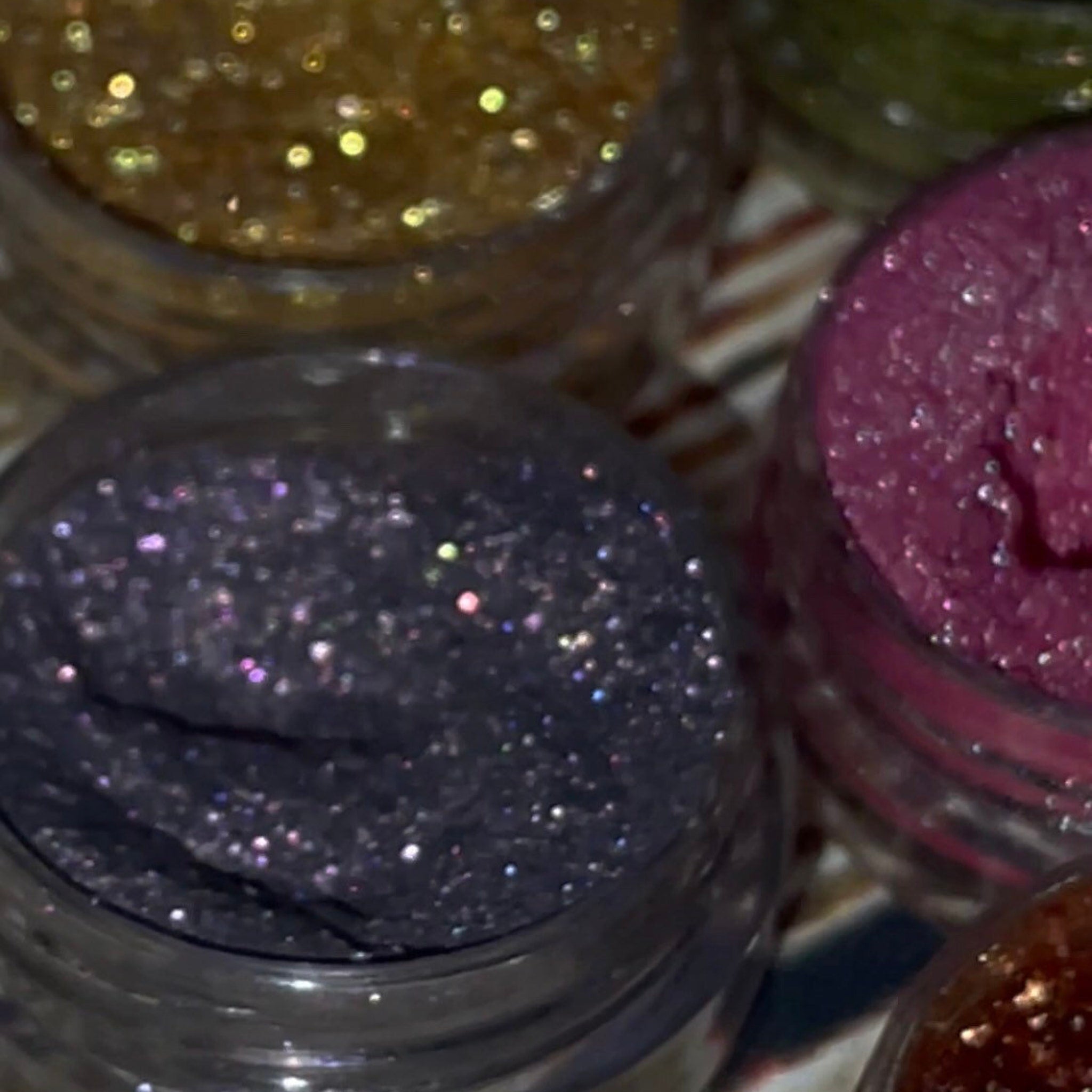 Side view of 12 shimmery vegan eyeshadows in round pans, showcasing vibrant colors and sleek black compact packaging
