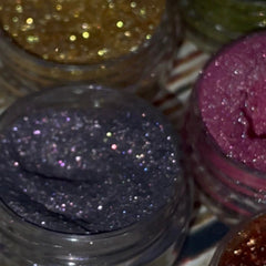 Side view of 12 shimmery vegan eyeshadows in round pans, showcasing vibrant colors and sleek black compact packaging