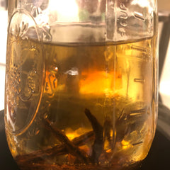 Glass jar with amber liquid, brown sticks, and measurement markings visible inside the glass jar