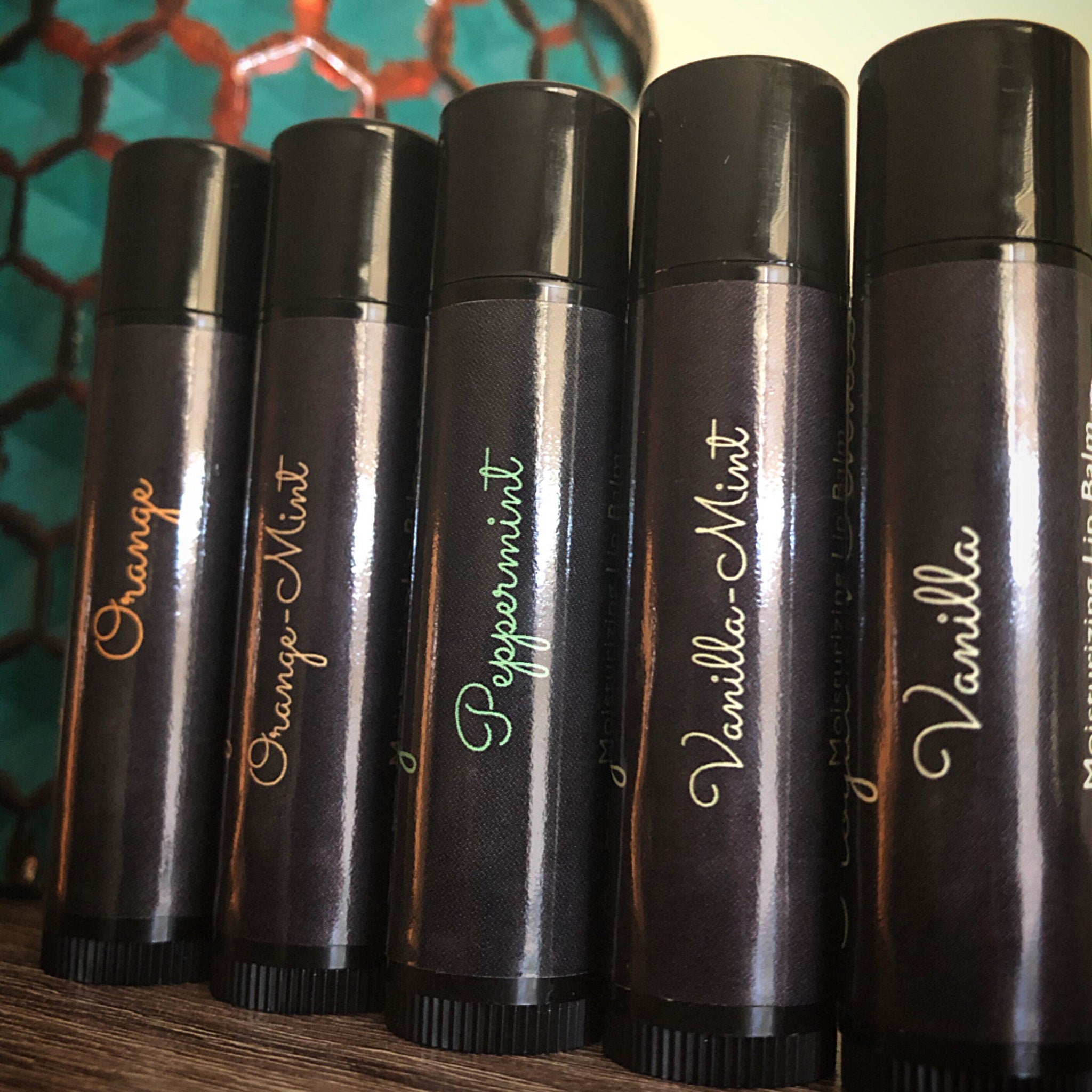 Lip balm tubes with black caps and labels, text in gold and green, on wooden surface