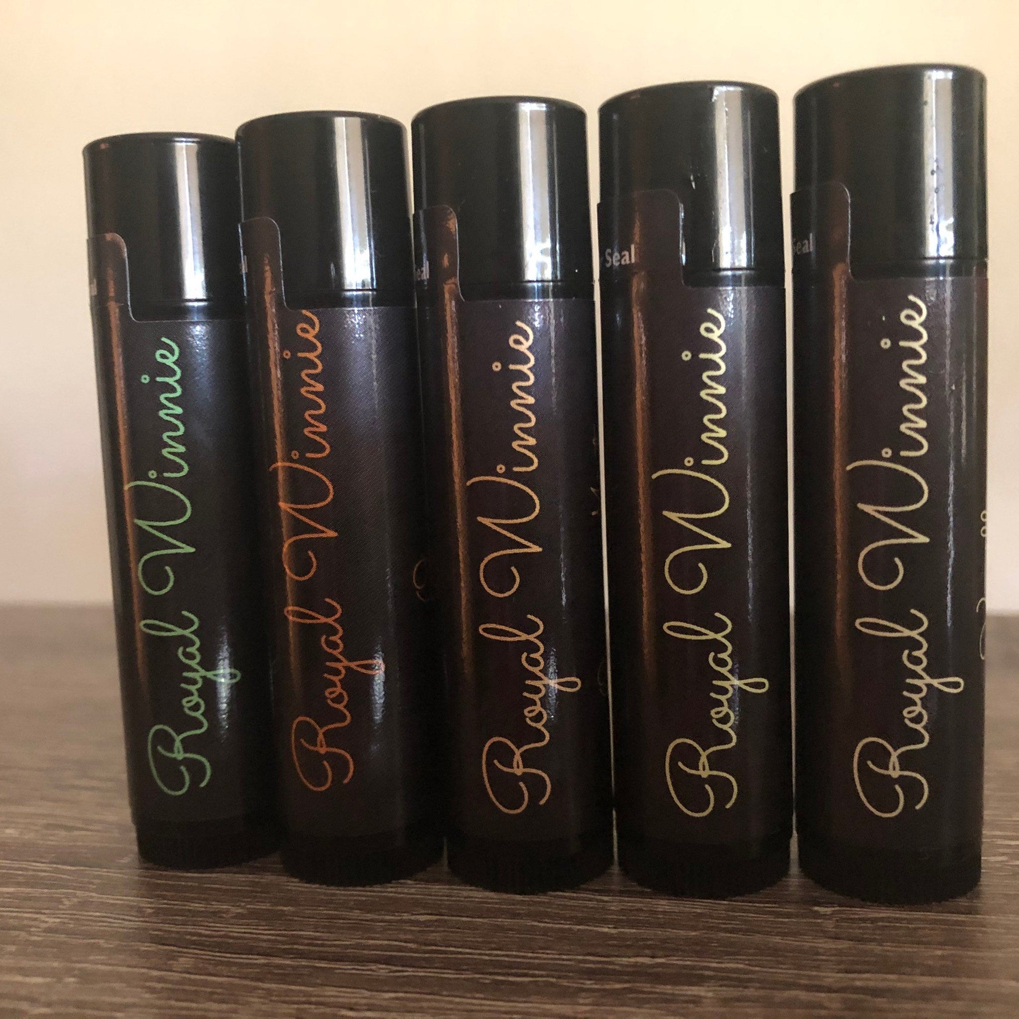 Lip balm tubes with black bodies, colorful "Royal Winnie" script, and black caps