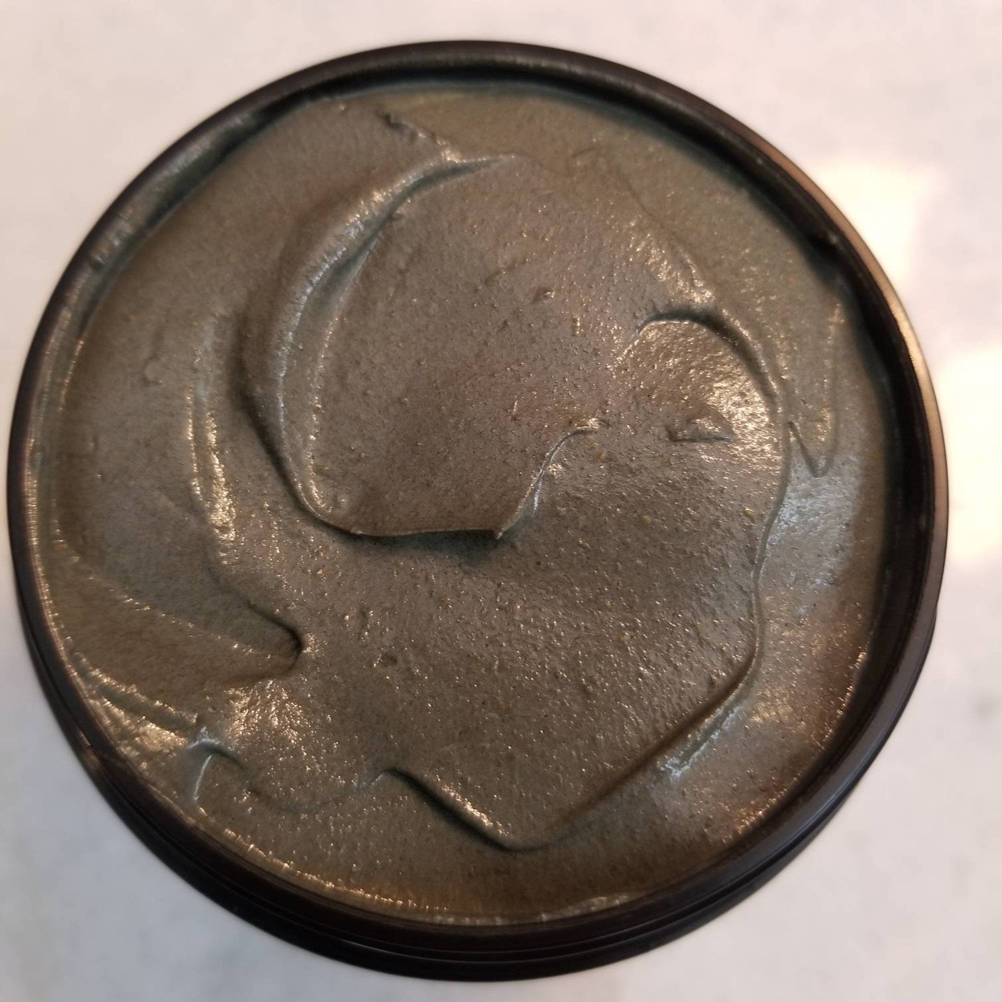 Side view of black glass jar with gold lid containing charcoal turmeric face mask, showcasing minimalist branding
