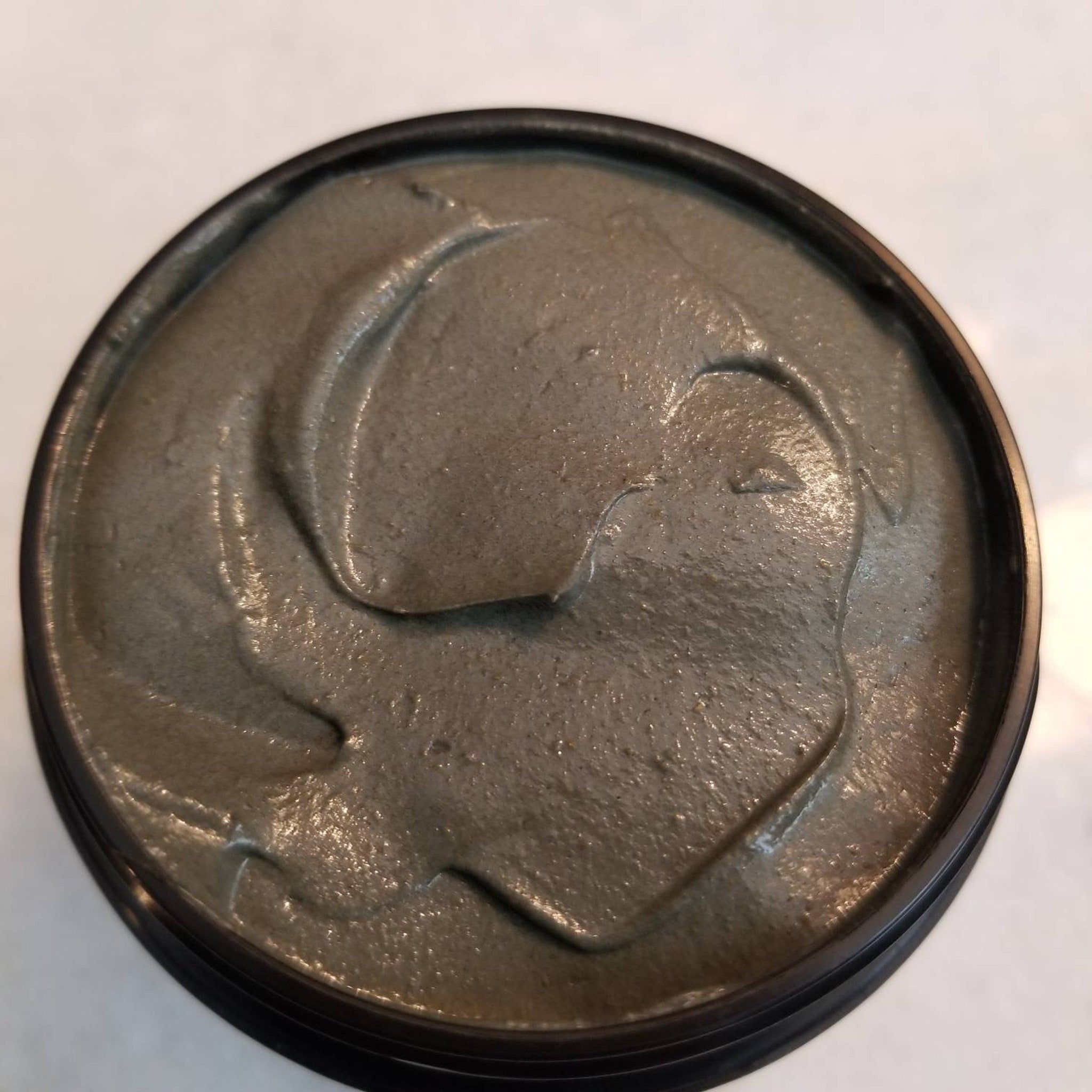 Black glass jar of charcoal turmeric face mask with gold lid, shown open revealing creamy dark gray formula