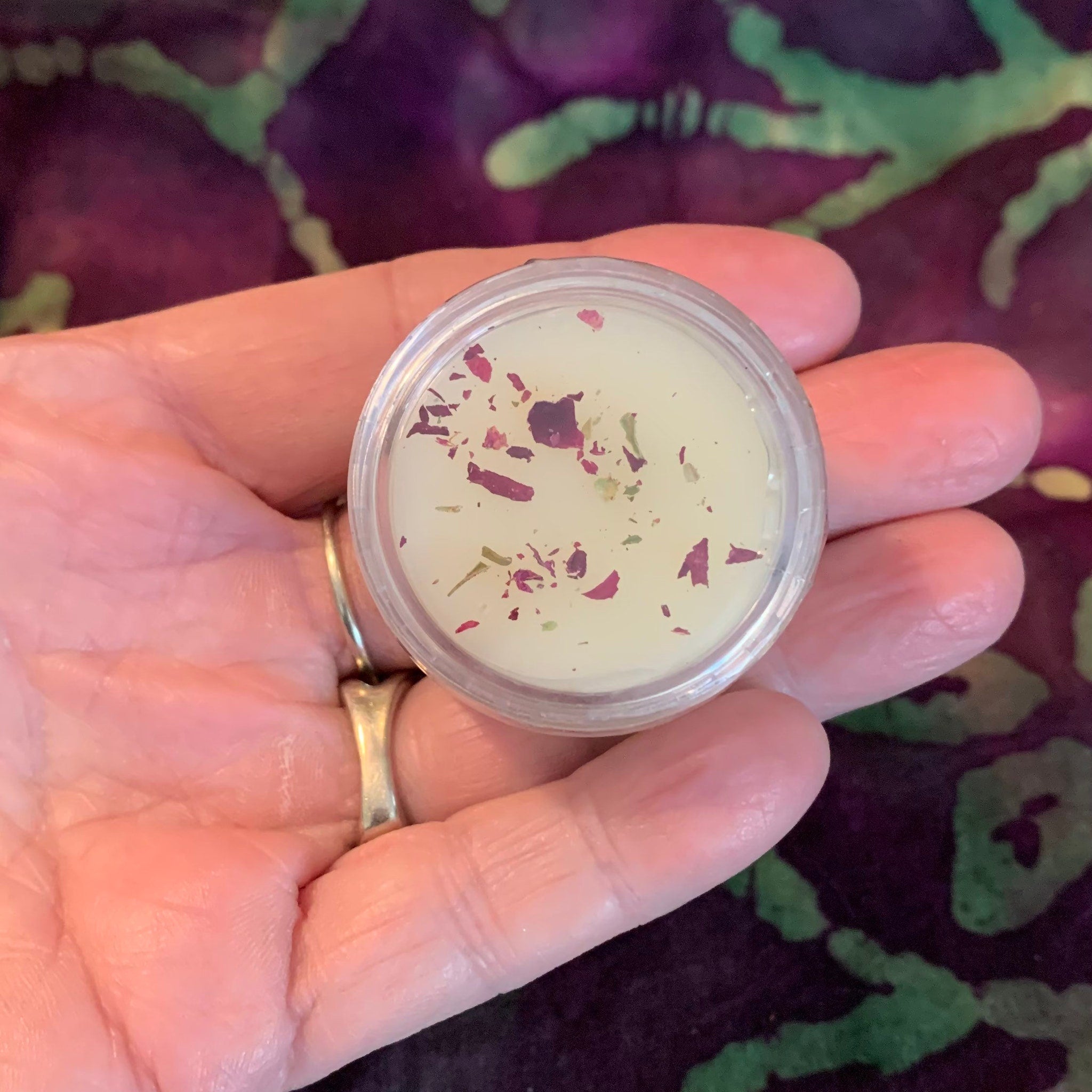Lip balm jar with yellow balm, red petals, and clear plastic container held in hand