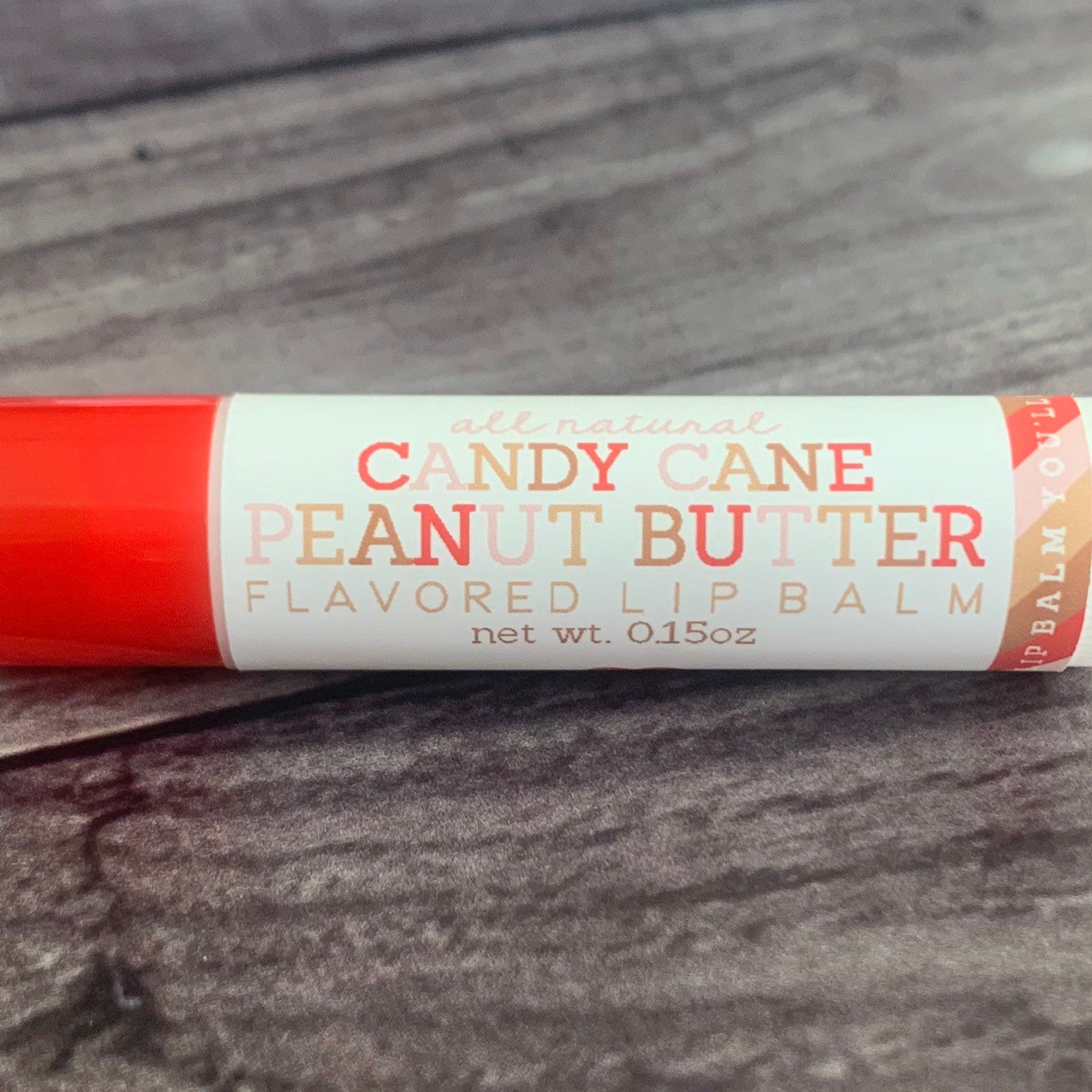 Lip balm tube with red and white label, Candy Cane Peanut Butter text, on wood grain background
