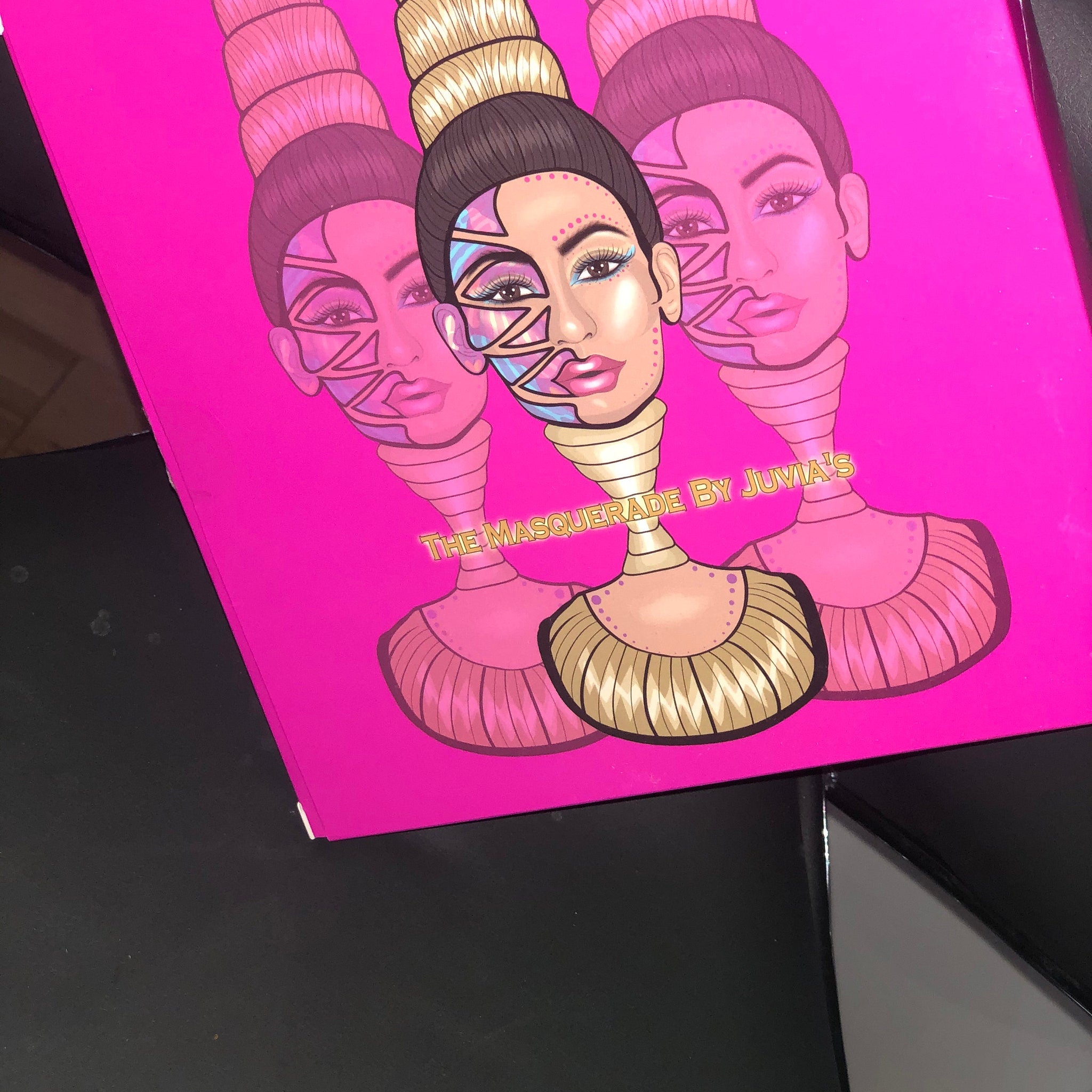 Makeup palette with pink background, illustrated faces, and "The Masquerade by Juvia's" text
