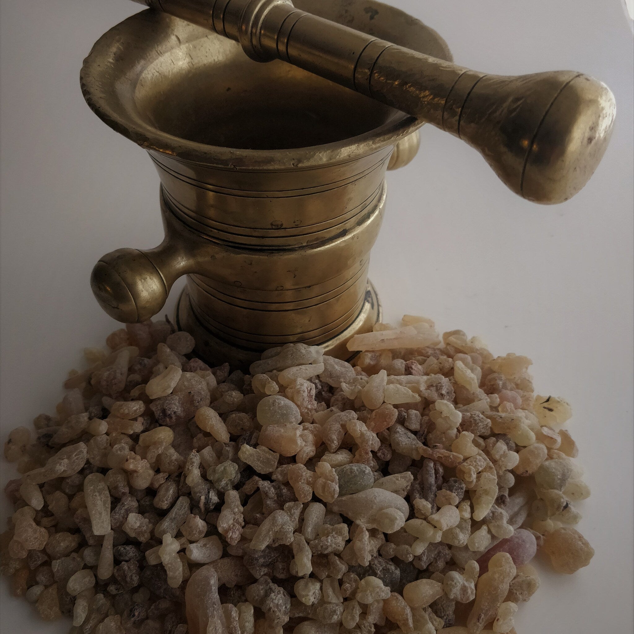 Brass mortar and pestle with light brown and tan granules, on white surface