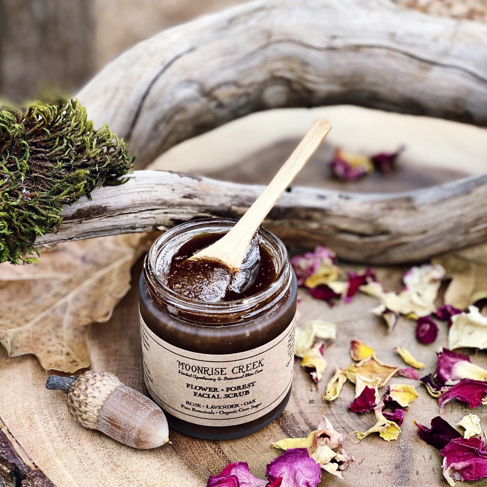 Facial scrub jar with dark brown contents, wooden spoon, and Moonrise Creek label on wood surface