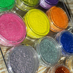 Side view of 12 shimmery vegan eyeshadows in round pans showcasing vibrant pigments and metallic finishes