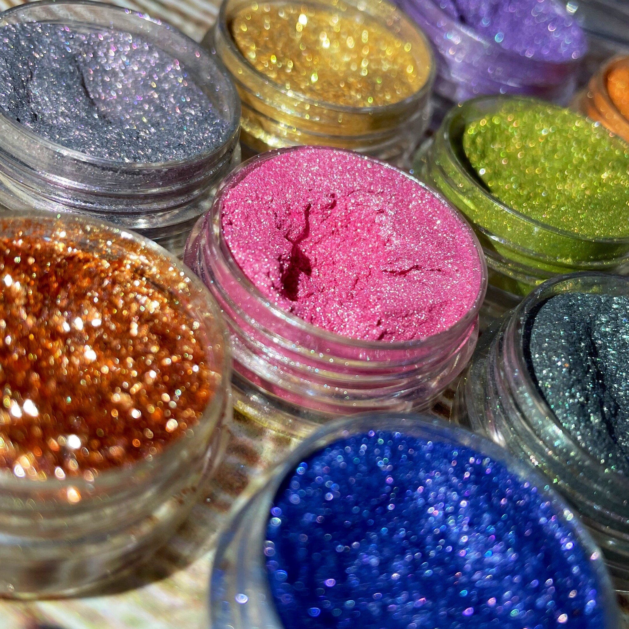 Side view of 12 shimmery vegan eyeshadows in round pans showing vibrant colors and reflective finishes