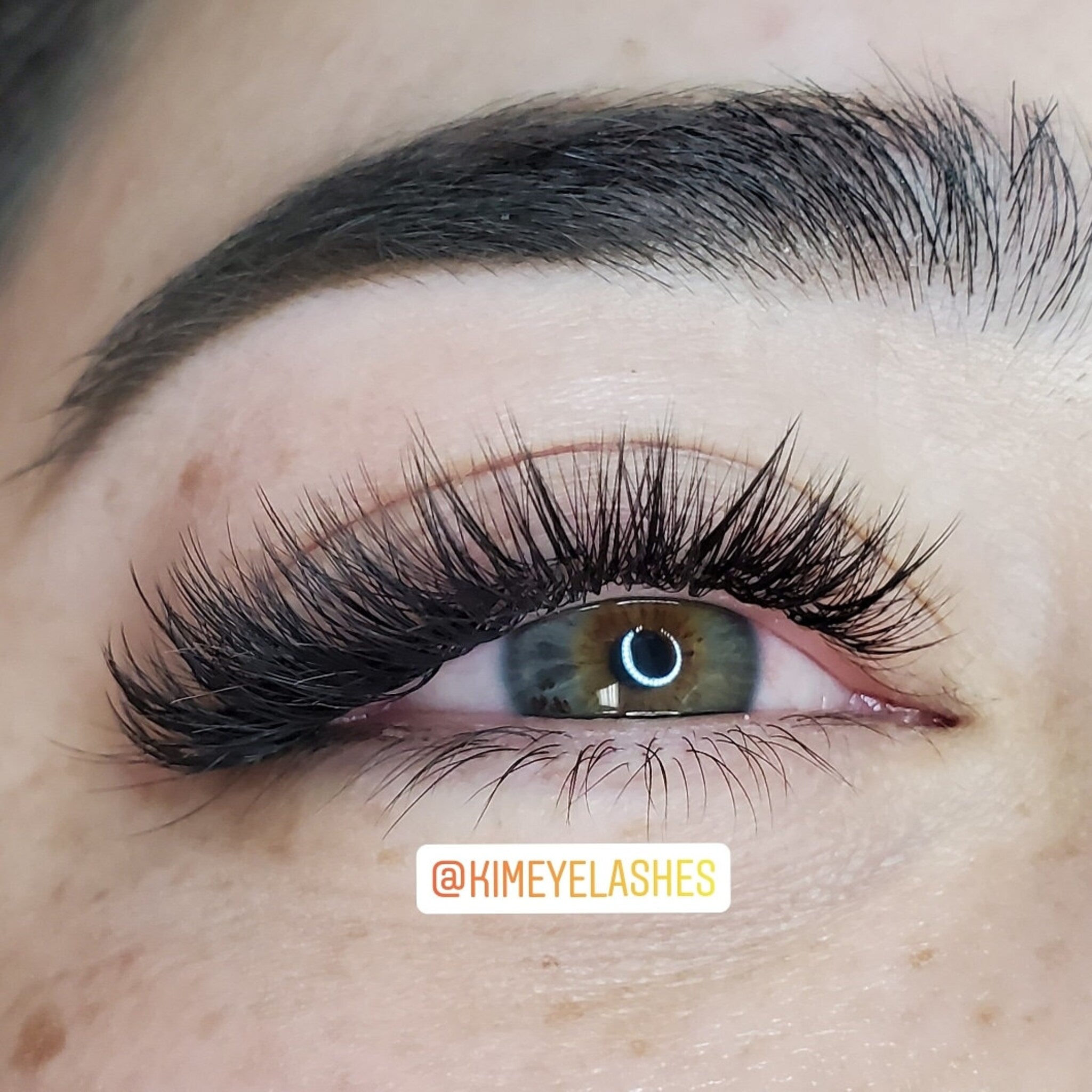 Eyelash extensions with black lashes, dark eyebrows, and visible eye with @KIMEYELASHES text