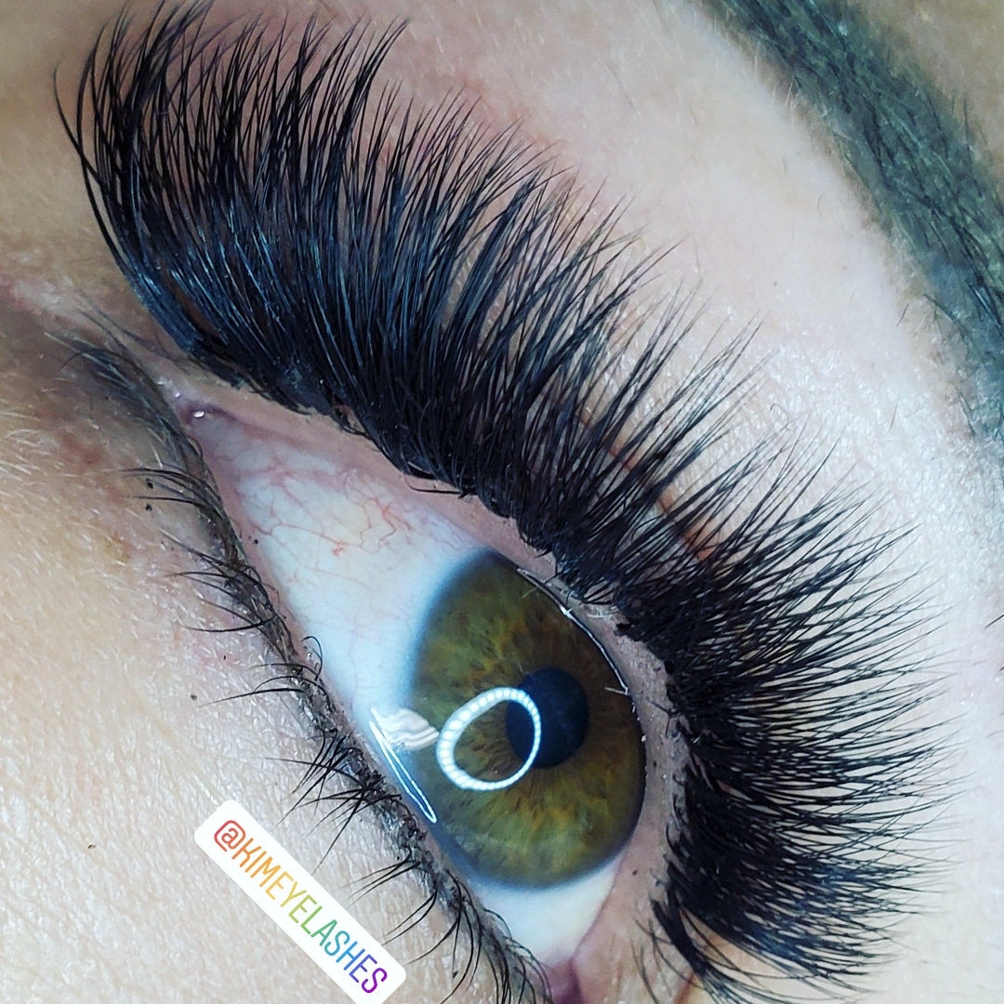 Eyelash extensions with long, black, wispy lashes and visible eye with @KIMEYELASHES text