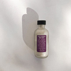 Facial exfoliant bottle, frosted glass, black cap, purple label with directions on white background