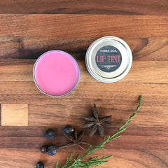 Lip tint in pink color, silver tin, Herbs Soil brand on wooden surface