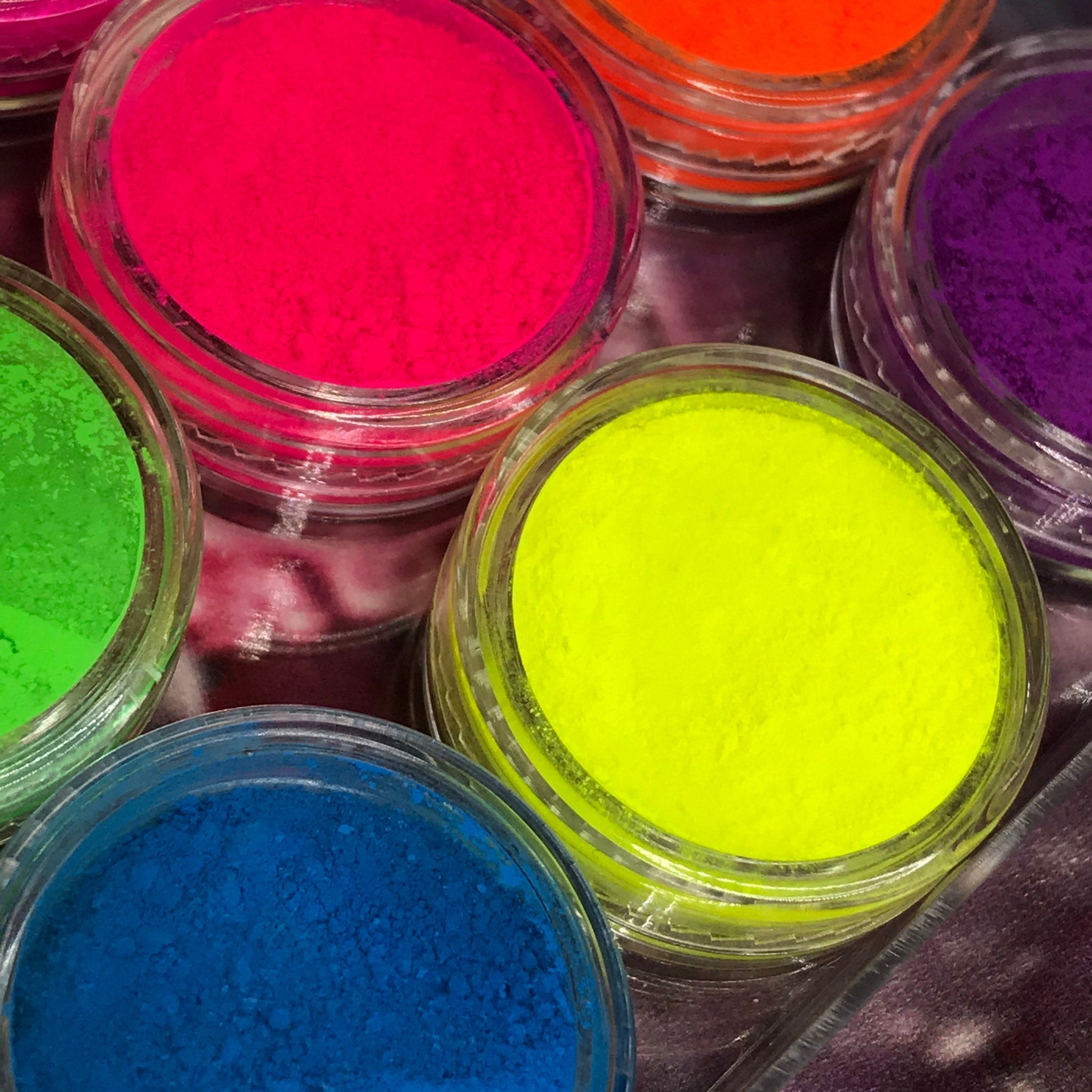 Close-up of vibrant neon pink and yellow matte eyeshadows in palette with smooth pressed powder texture