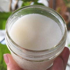White granular substance in a clear glass jar, held by a hand, close-up view