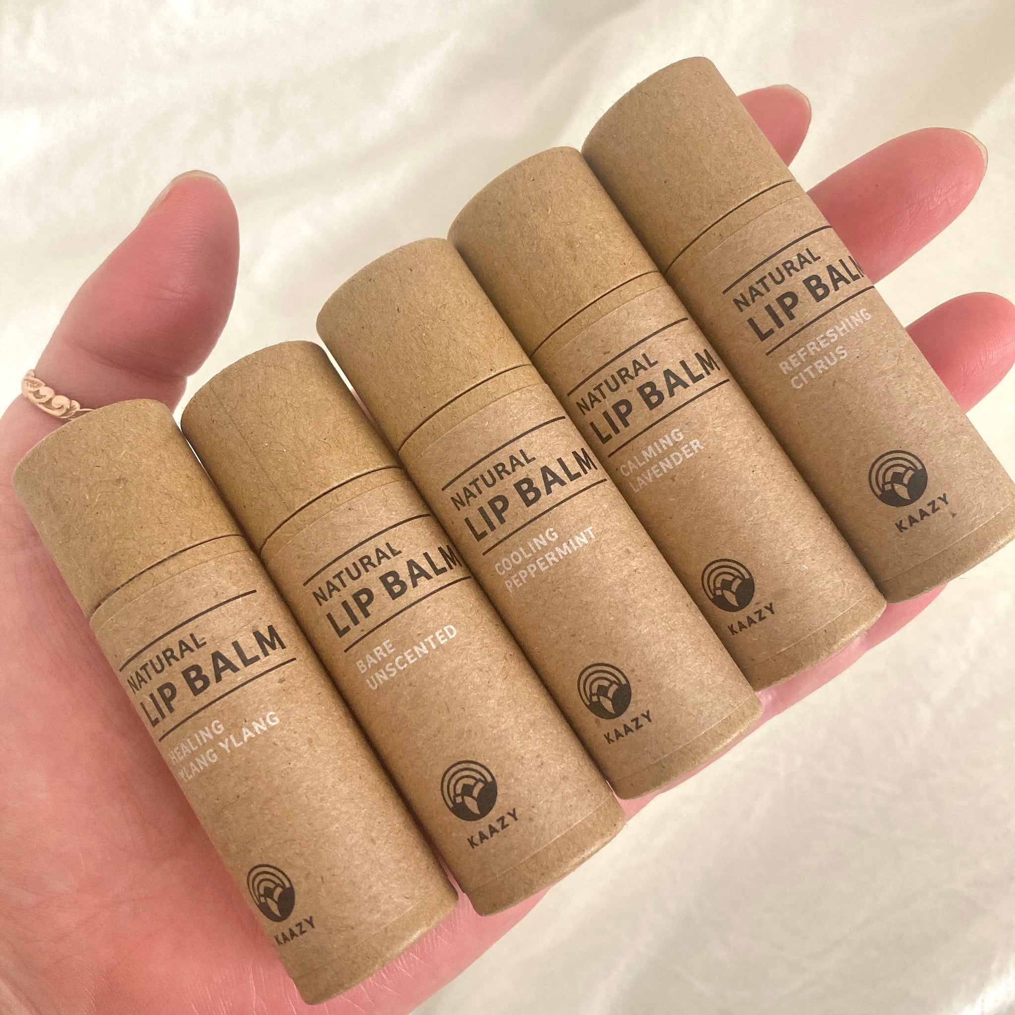 Lip balm tubes in brown cardboard, held in hand, with KAAZY brand text visible