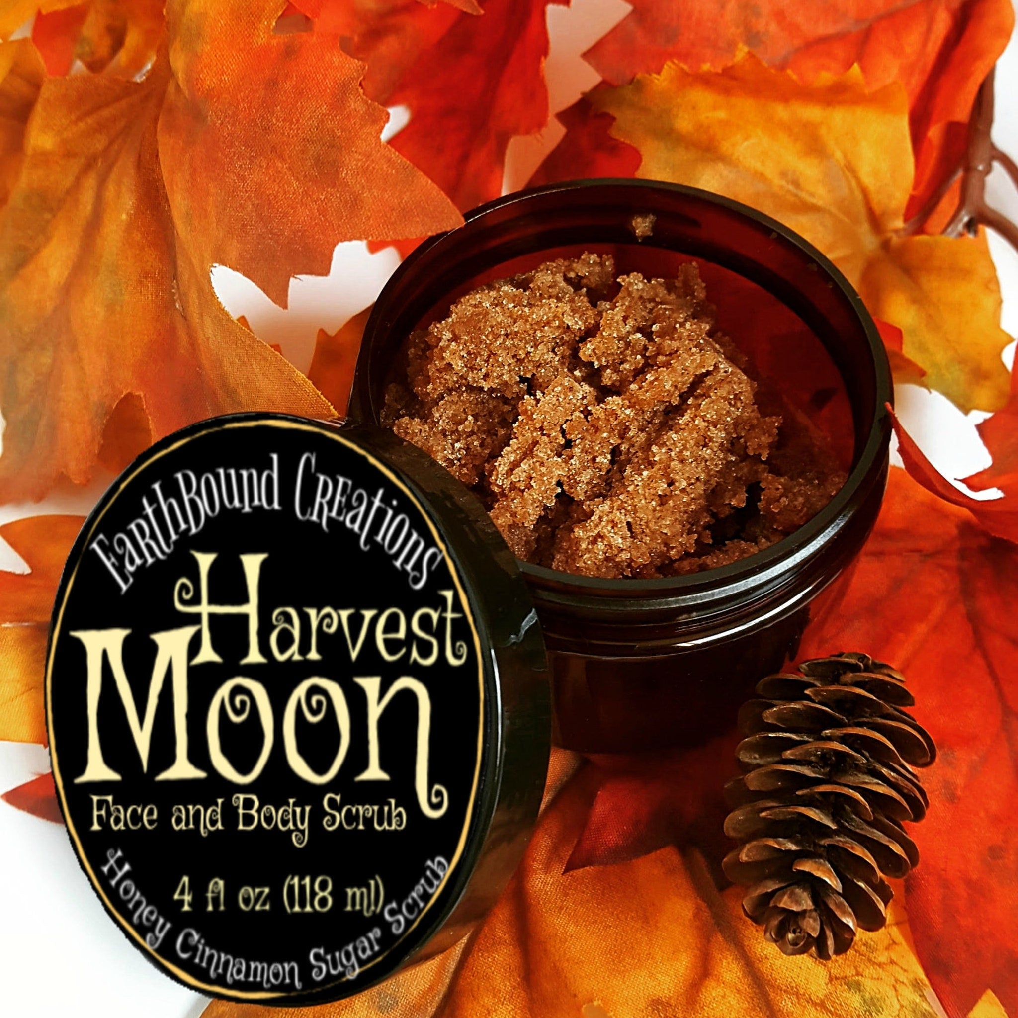 Face and body scrub in open black jar with brown granules, Harvest Moon label, and fall leaves background