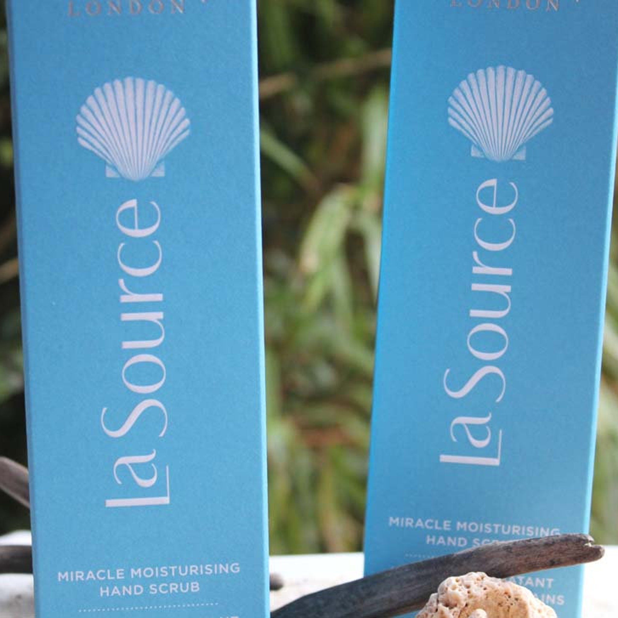 Hand scrub bottles, light blue with white seashell logo, "La Source" text visible