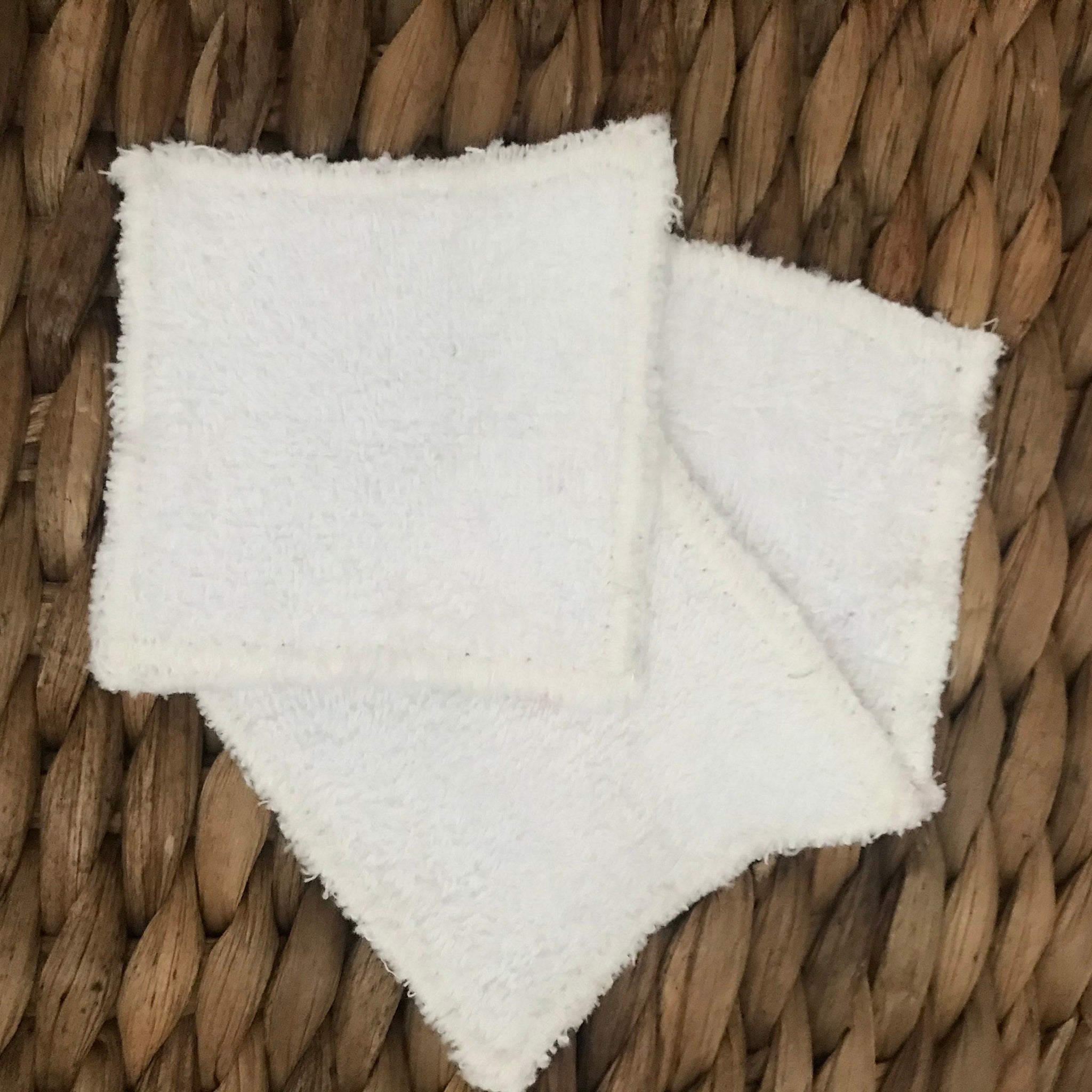 White washcloths, square, soft, on woven brown background
