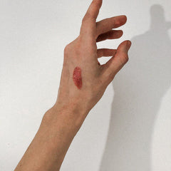 Lip color swatch, red glitter, on hand, against white background