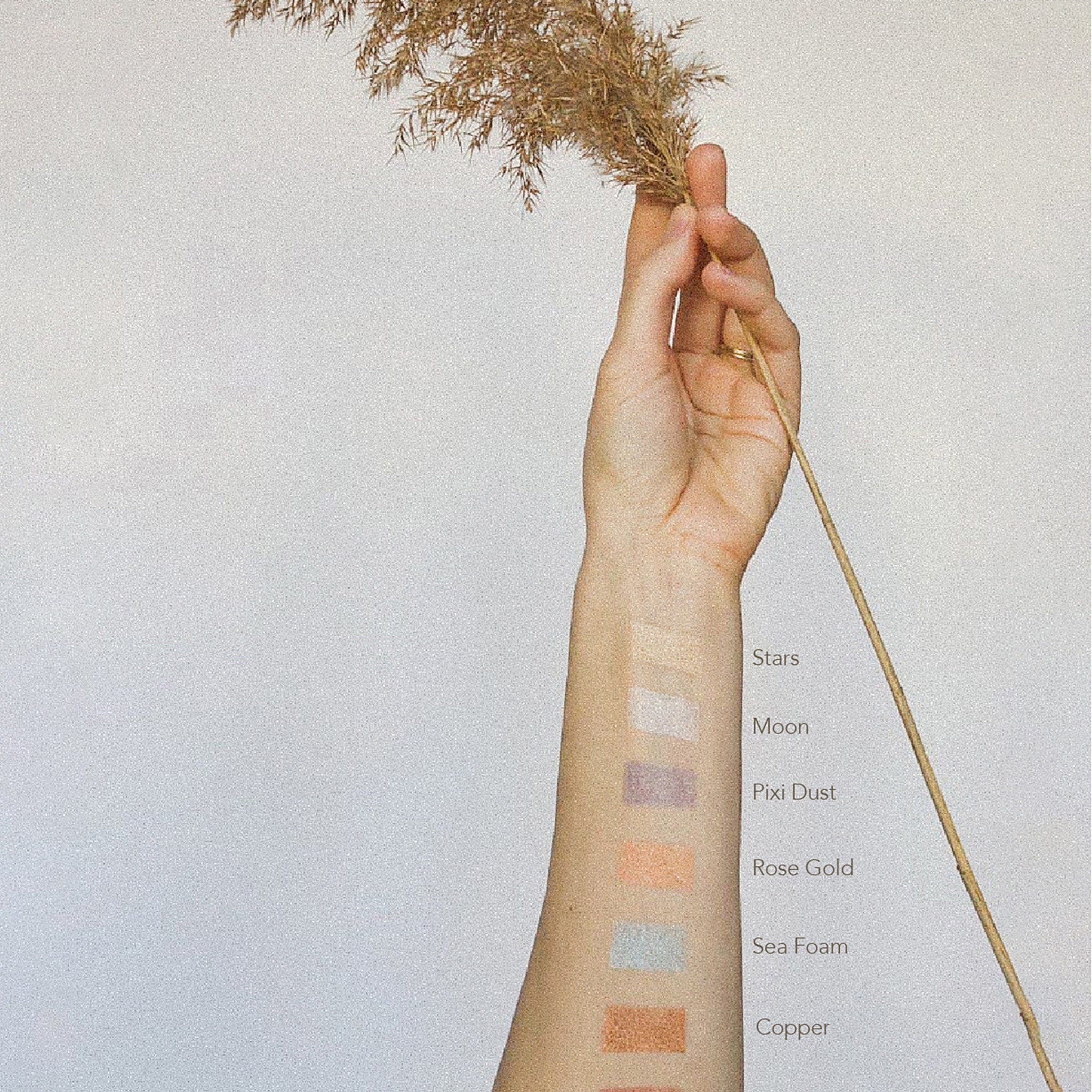 Swatches of eyeshadow colors in light shades on arm, with text labels and neutral background