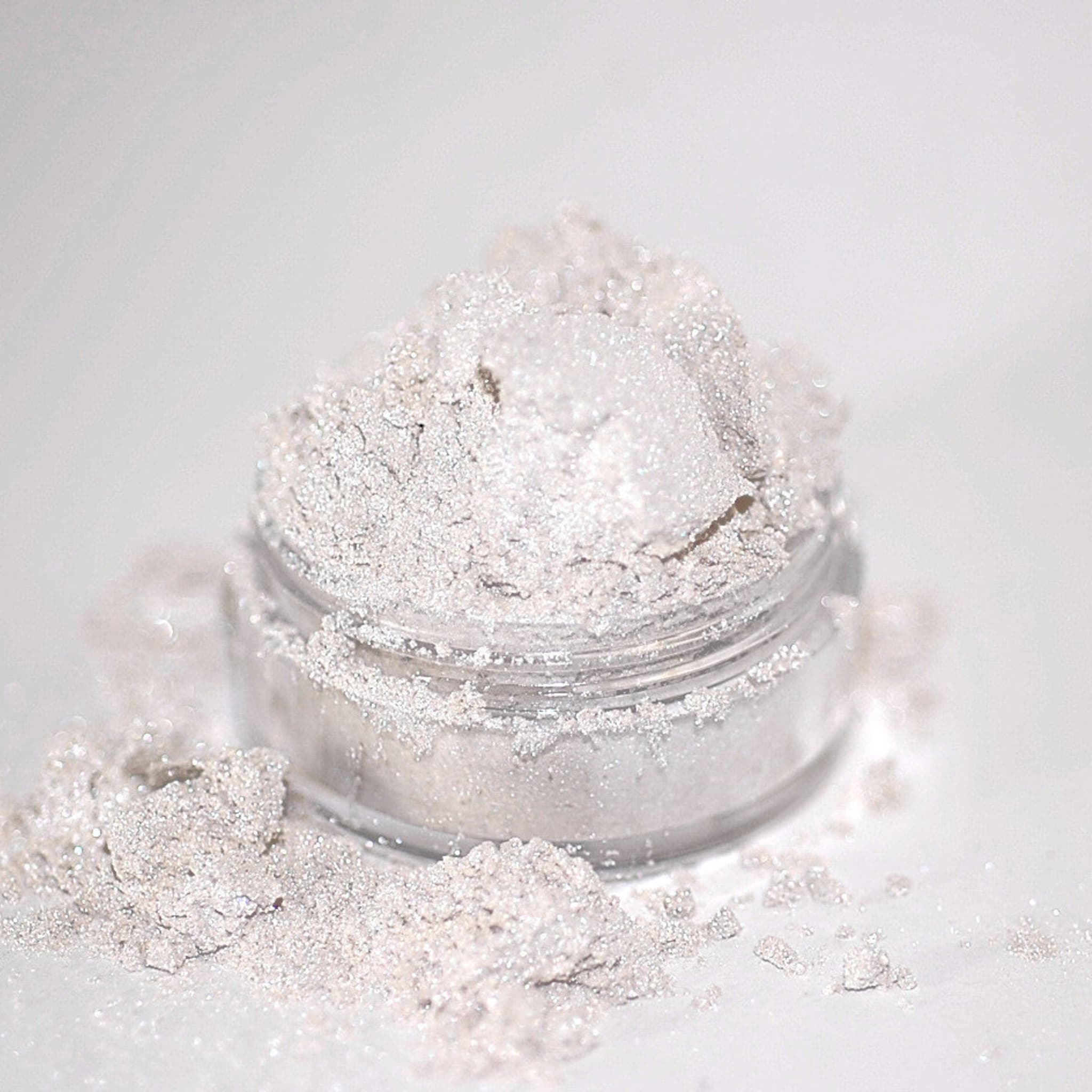 Glitter powder in a clear jar, silver and white, with spilled powder around it