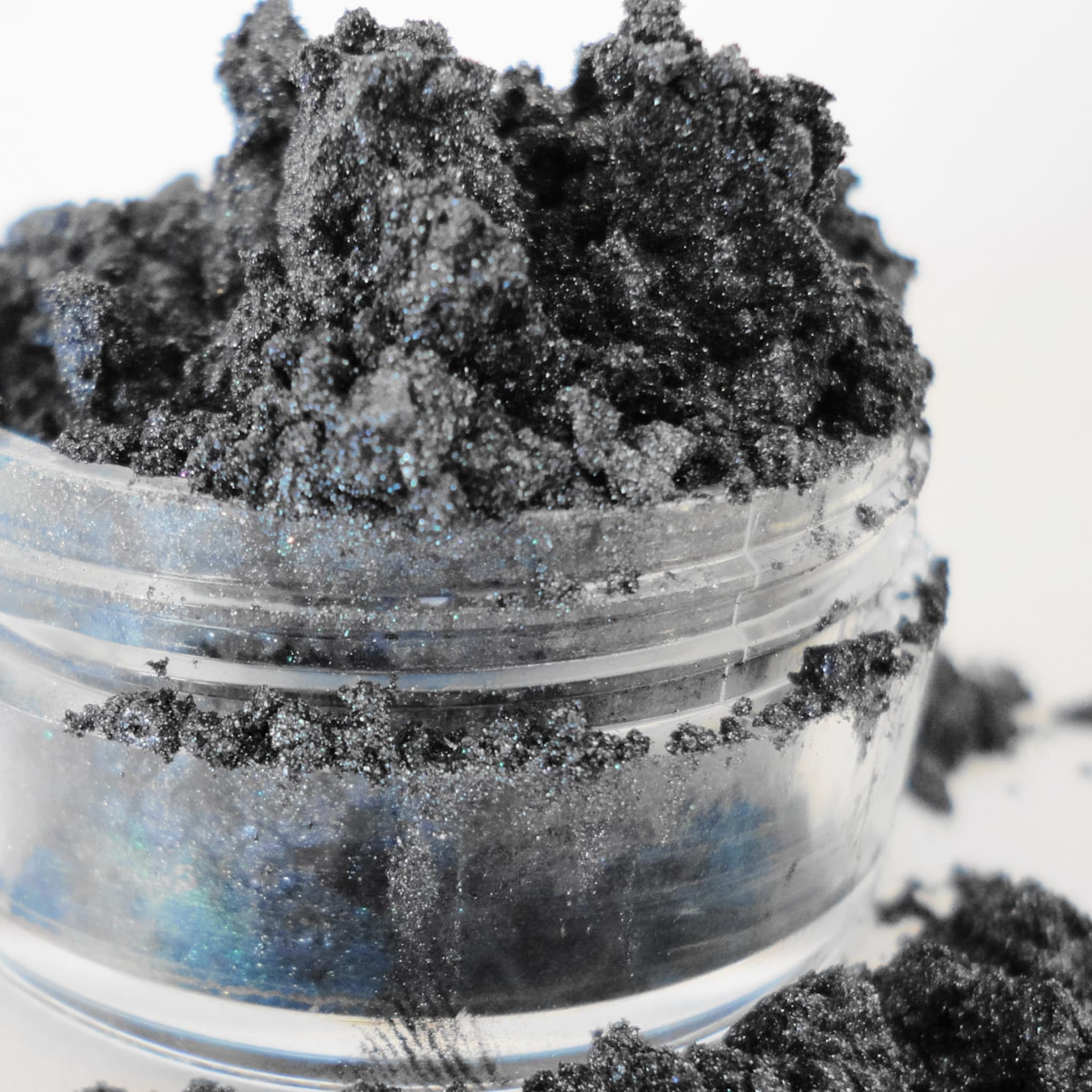 Black eyeshadow powder with glitter in a clear plastic container