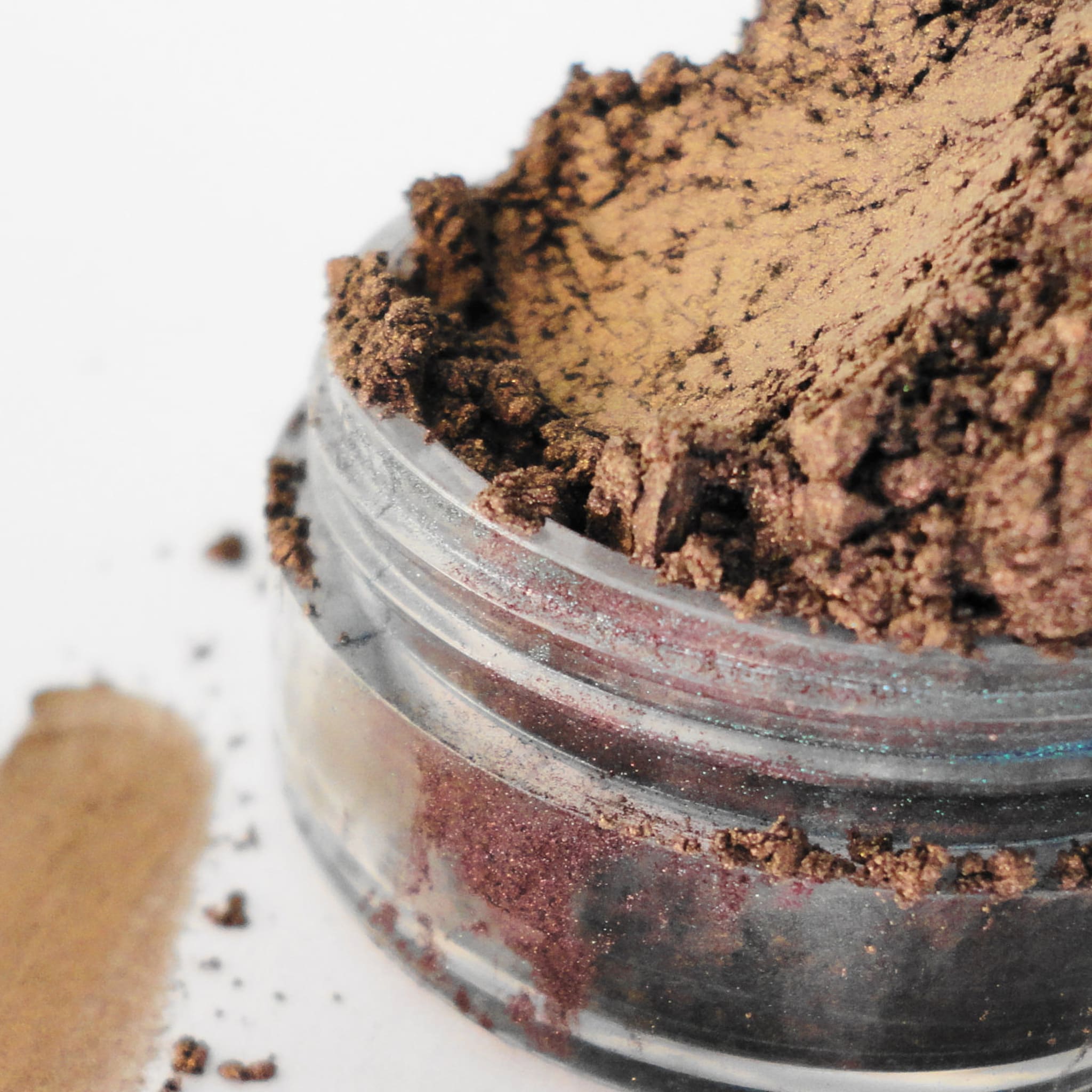 Eye shadow in brown and bronze shades with glitter in a clear jar, close-up view
