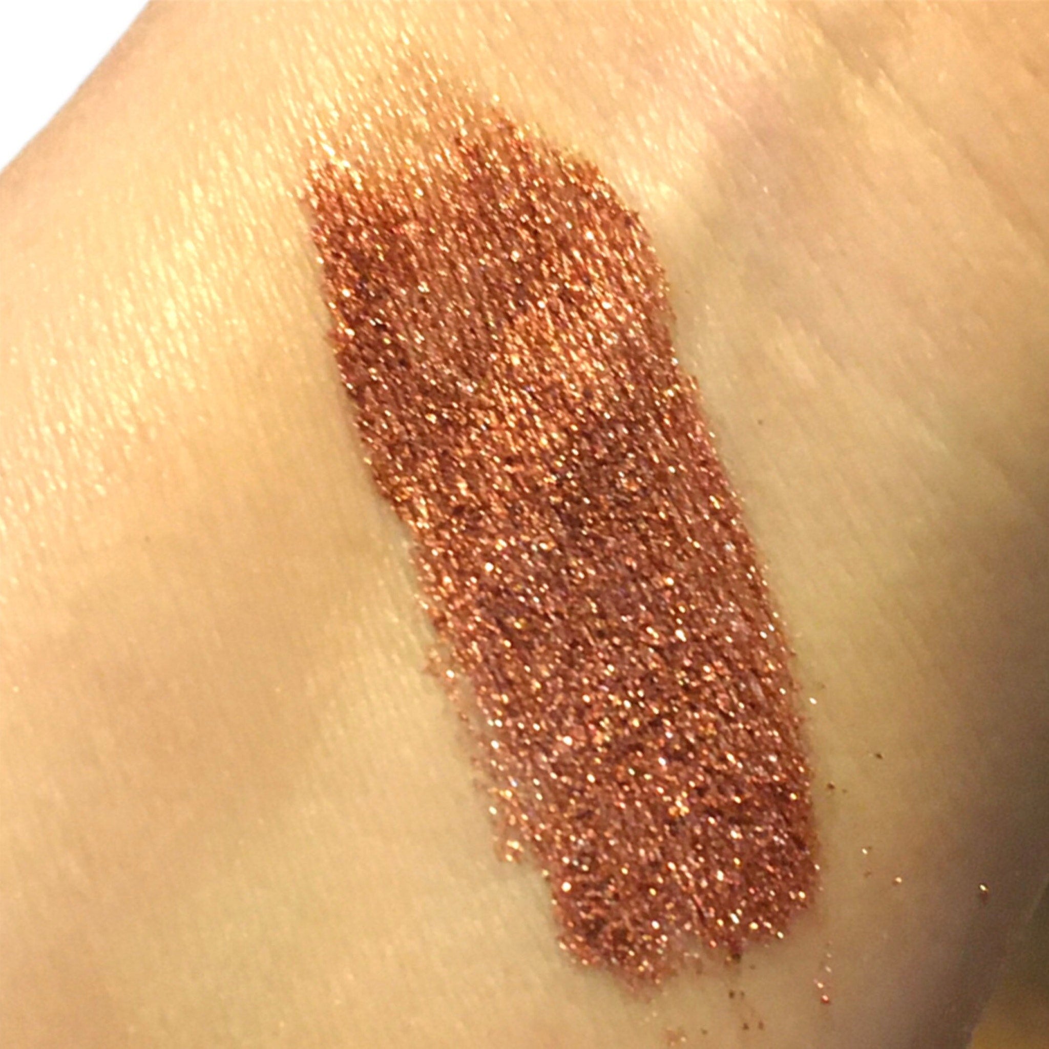 Glitter makeup swatch in copper color with sparkling texture on skin