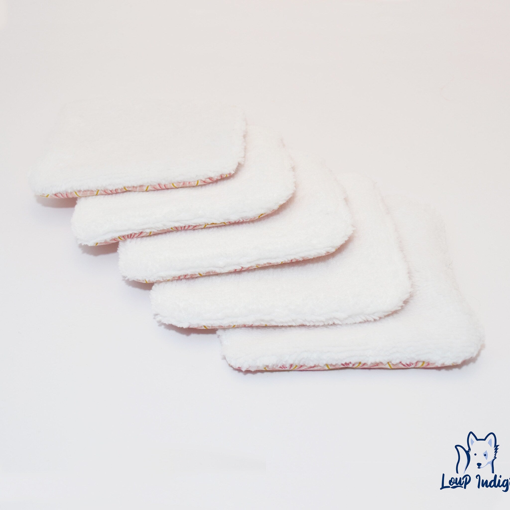 Reusable white fabric pads with pink and yellow trim, stacked on white surface