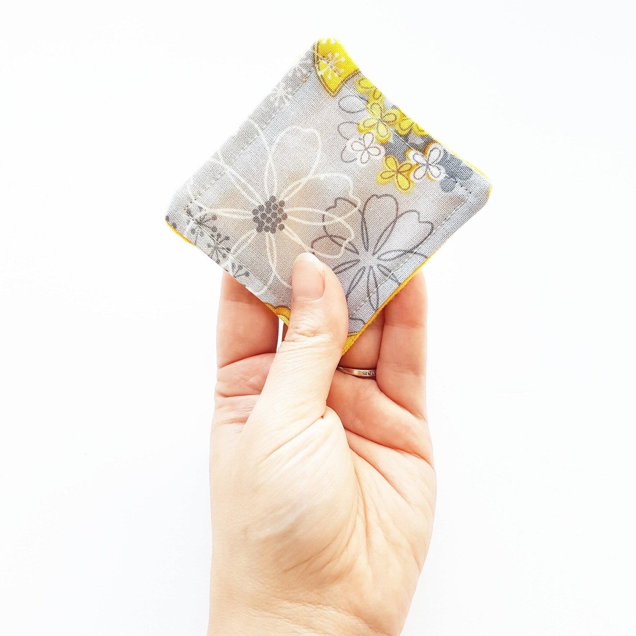 Reusable fabric square with floral pattern, gray and yellow colors, held by hand
