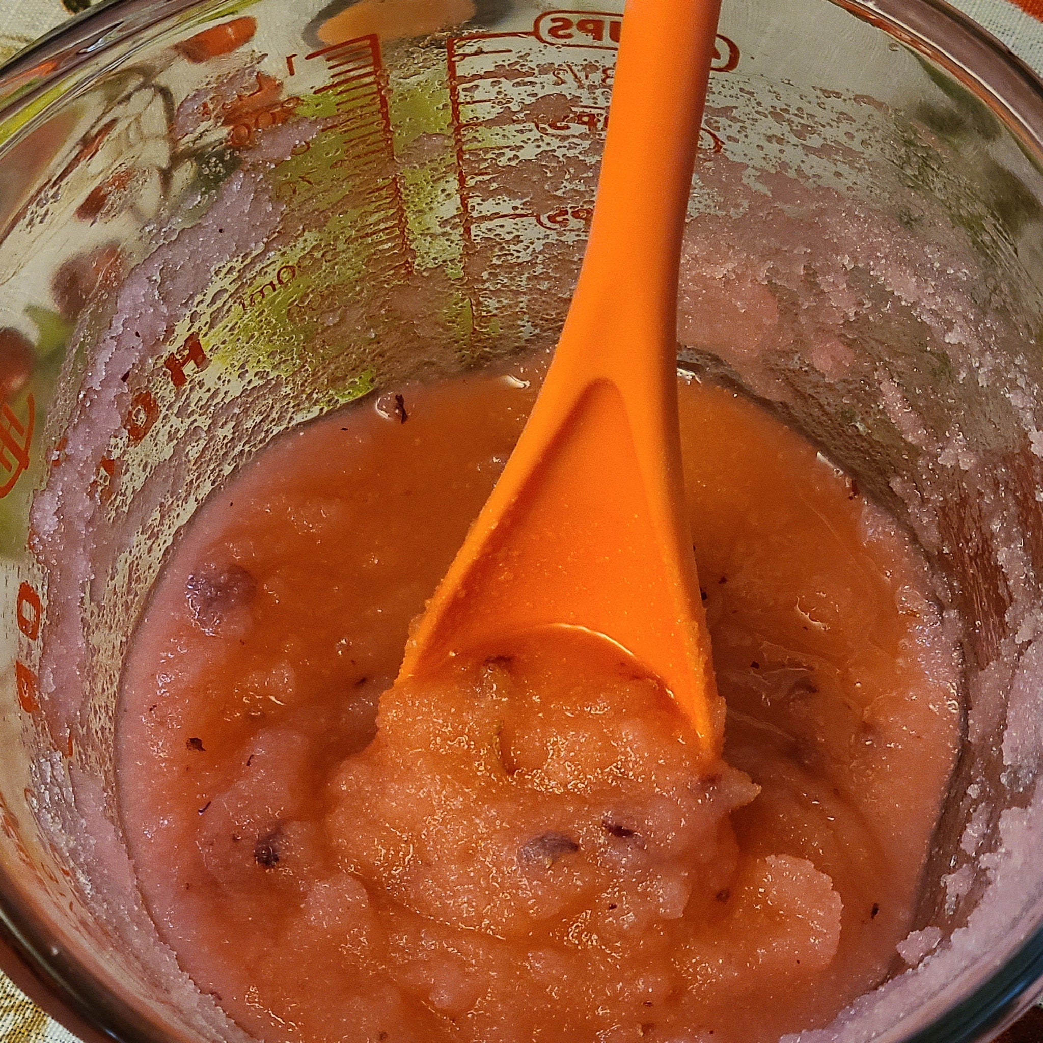 Orange spoon in pinkish-orange liquid, inside a clear glass measuring cup with red markings