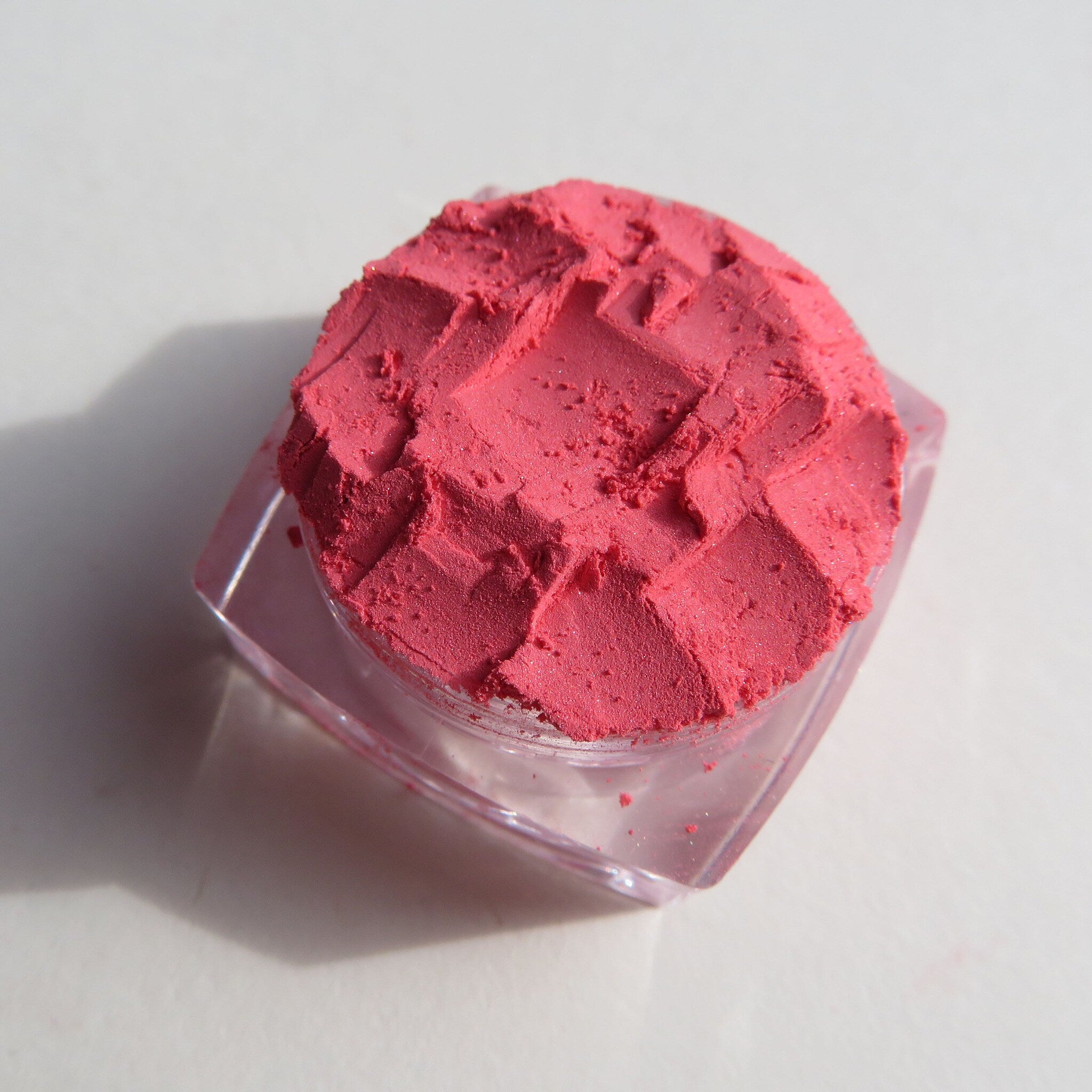 Close-up of matte coral pink loose mineral eyeshadow powder with soft texture in a small jar