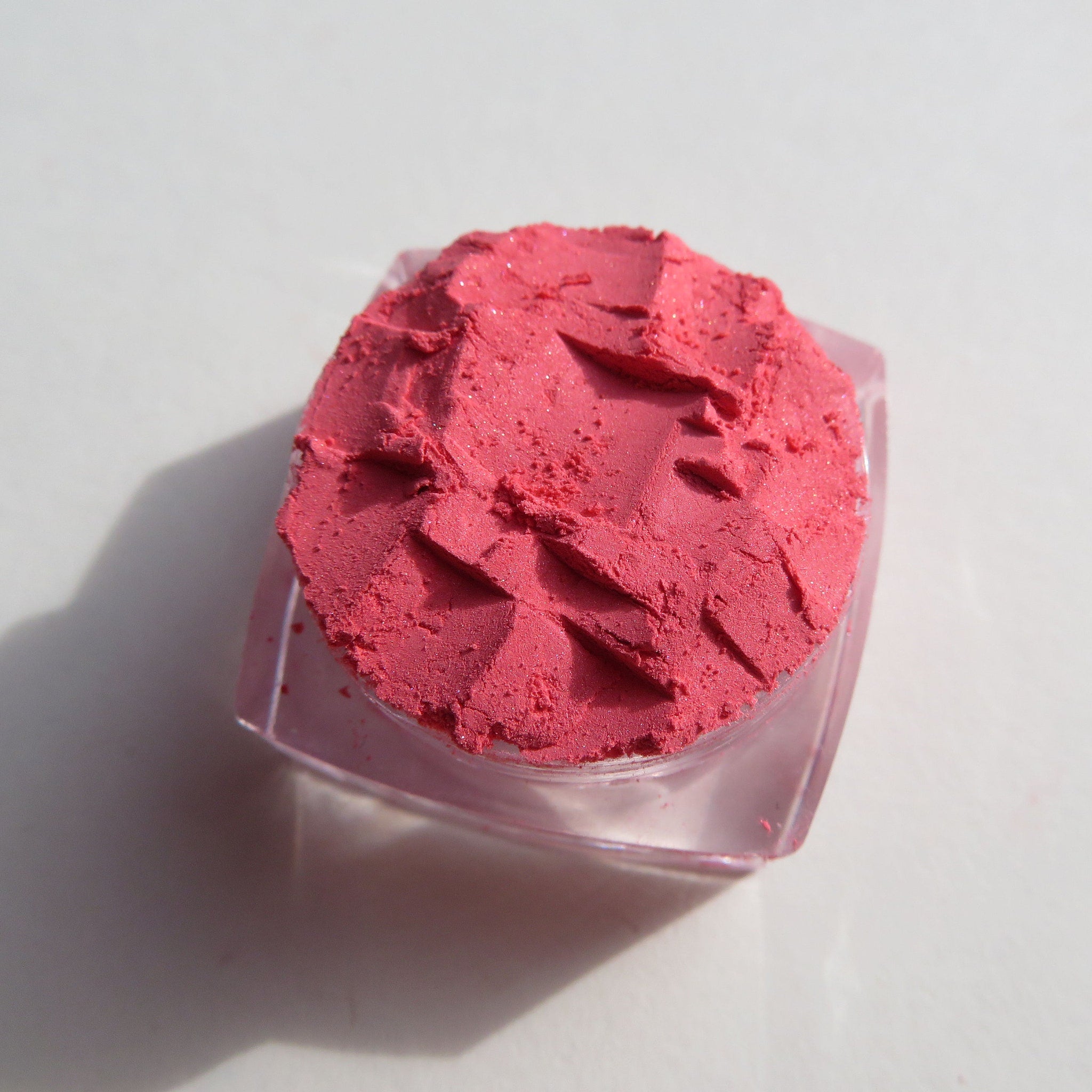 Side view of matte coral pink loose mineral eyeshadow in a sifter jar with black lid, showing fine powder texture